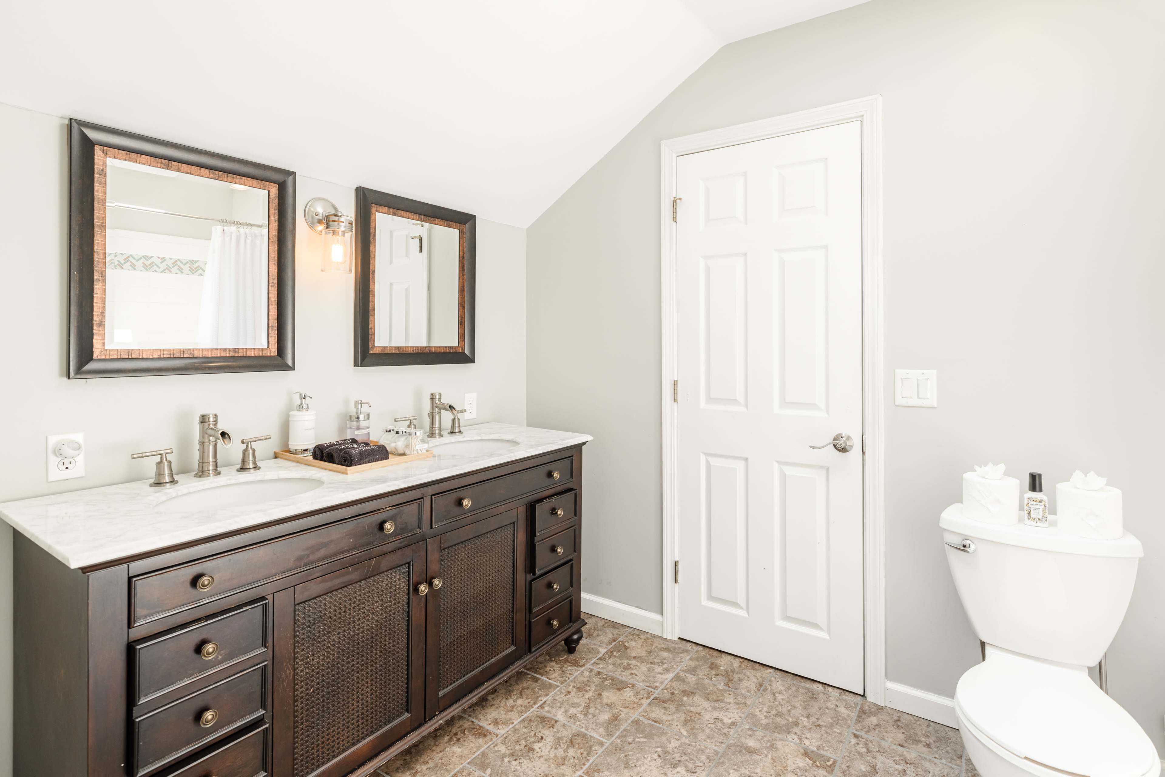 A bathroom featuring a double vanity with mirrors, a white toilet, and gray walls.