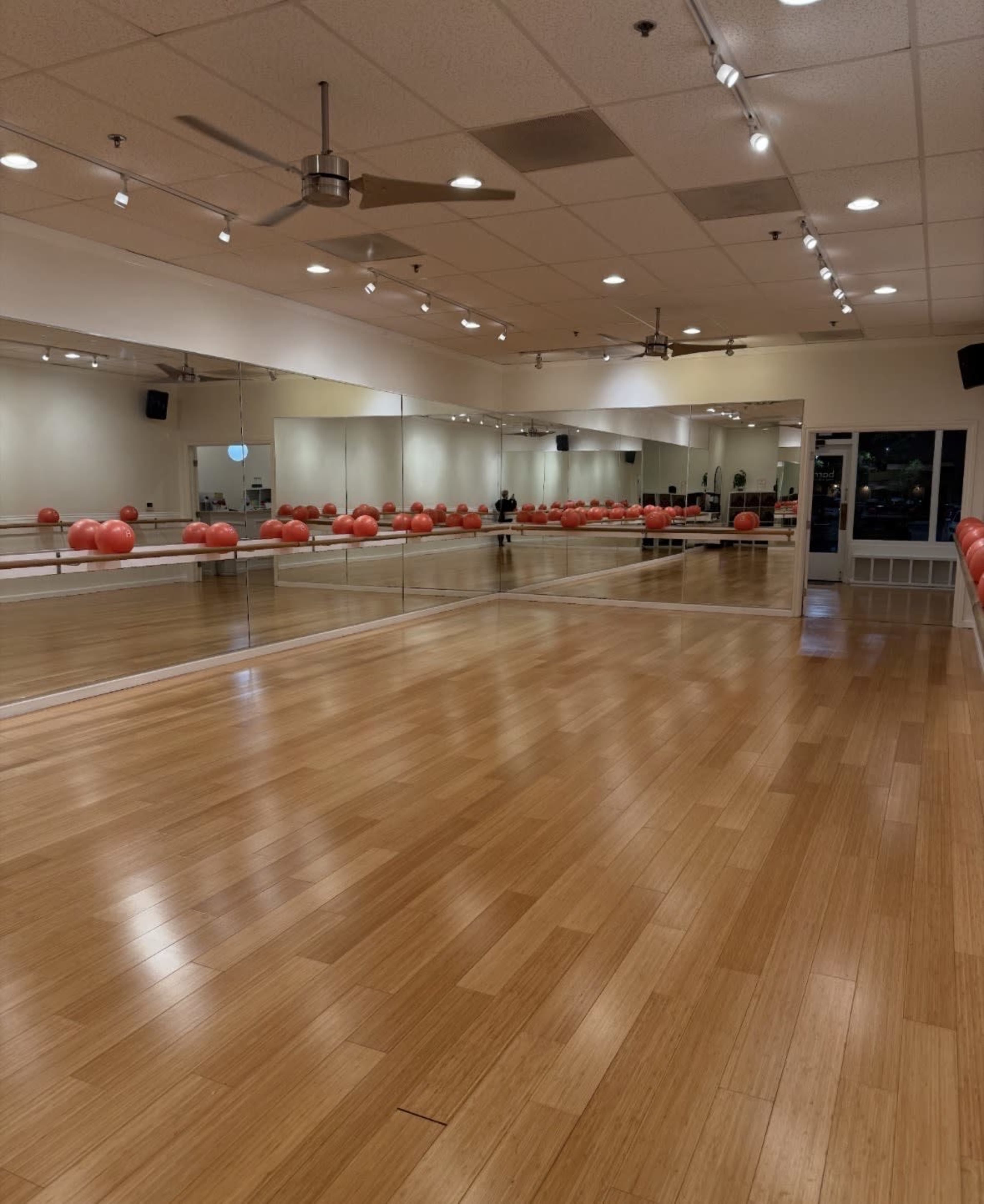 A spacious exercise studio features wooden flooring, large mirrors, and exercise balls arranged along one wall.