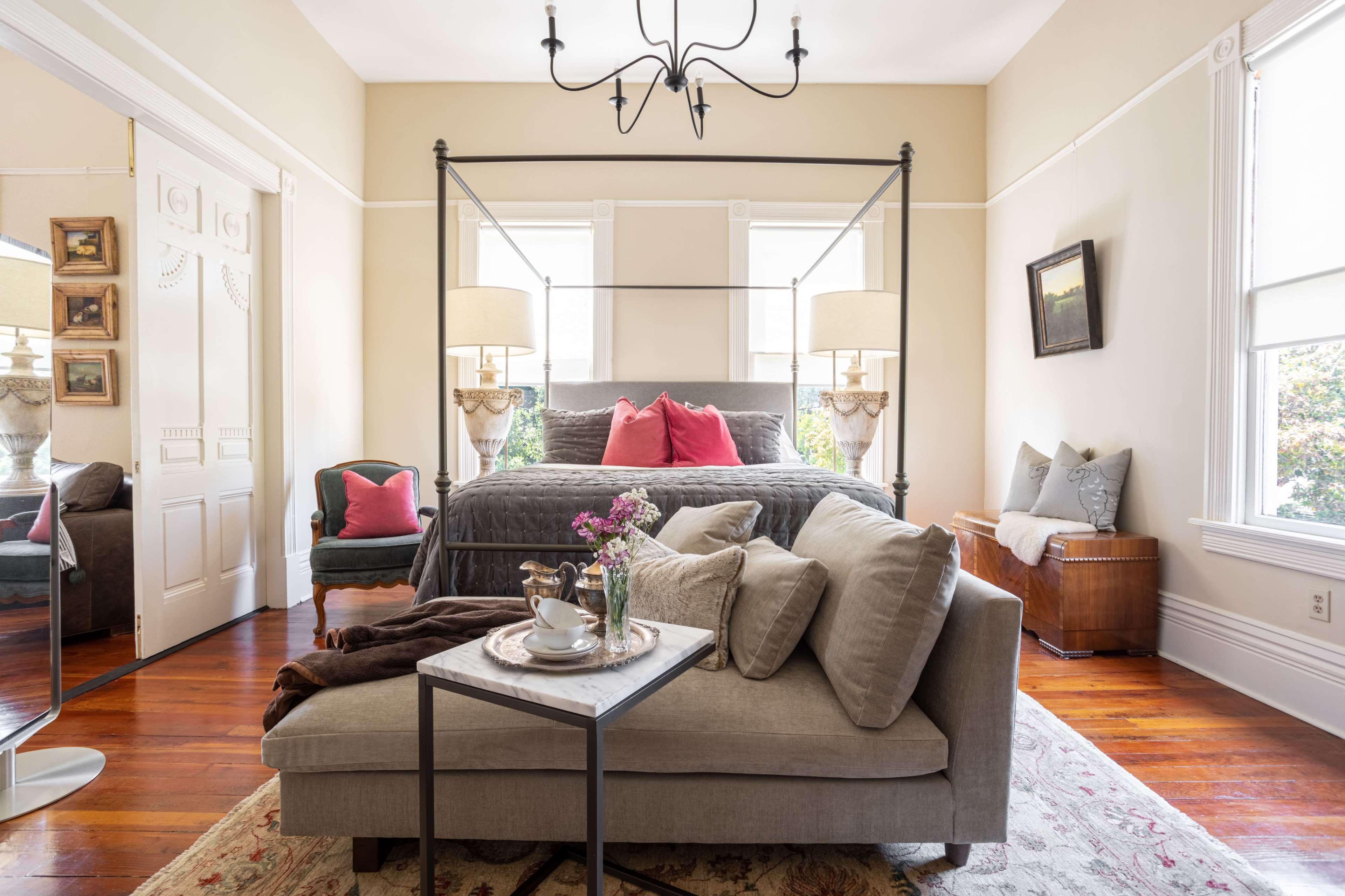 A well-furnished bedroom featuring a four-poster bed, a cozy seating area, and natural light streaming through large windows.