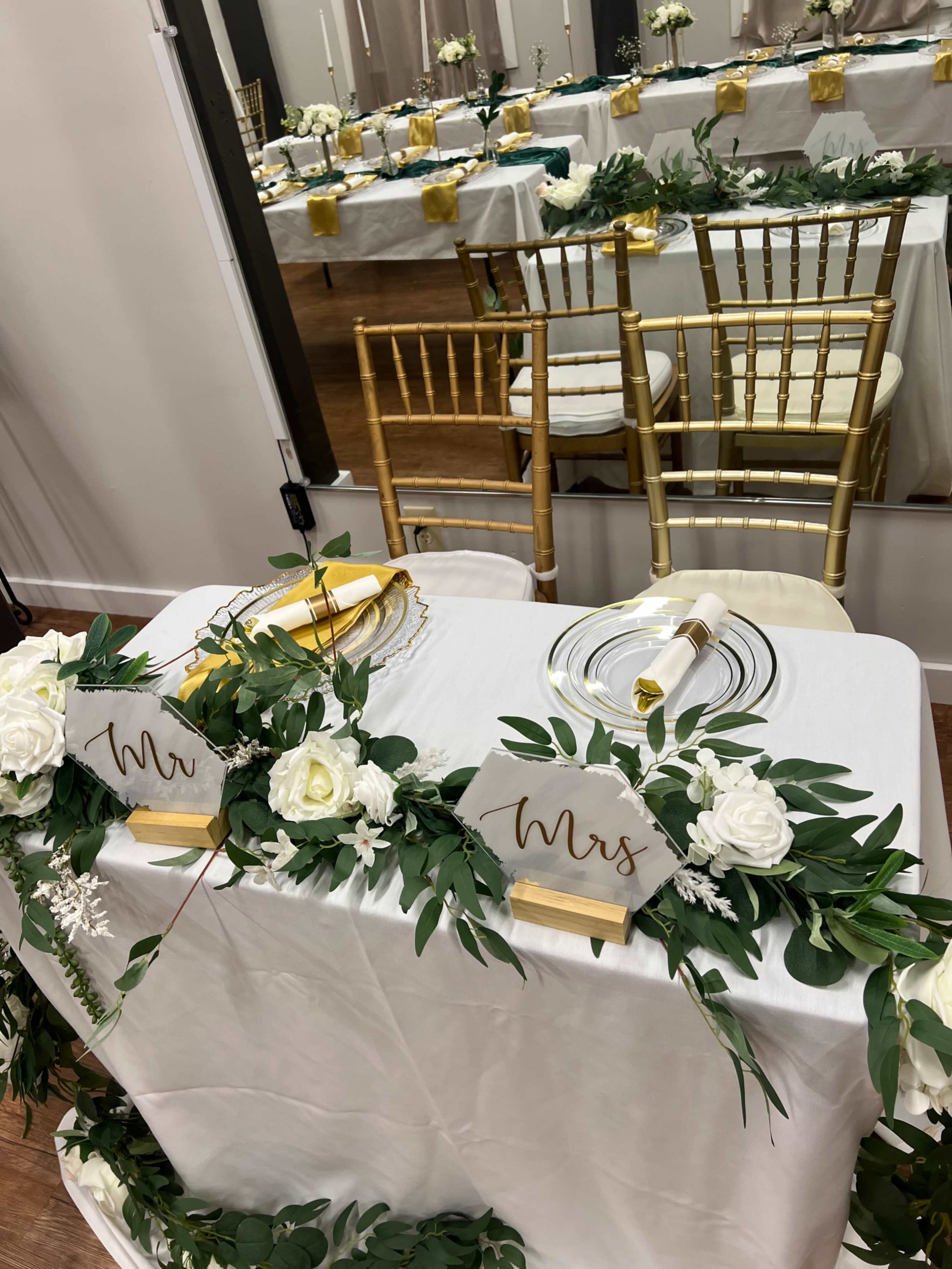 A beautifully decorated head table for a wedding features floral arrangements and signs labeled "Mr." and "Mrs." among elegant dinnerware.