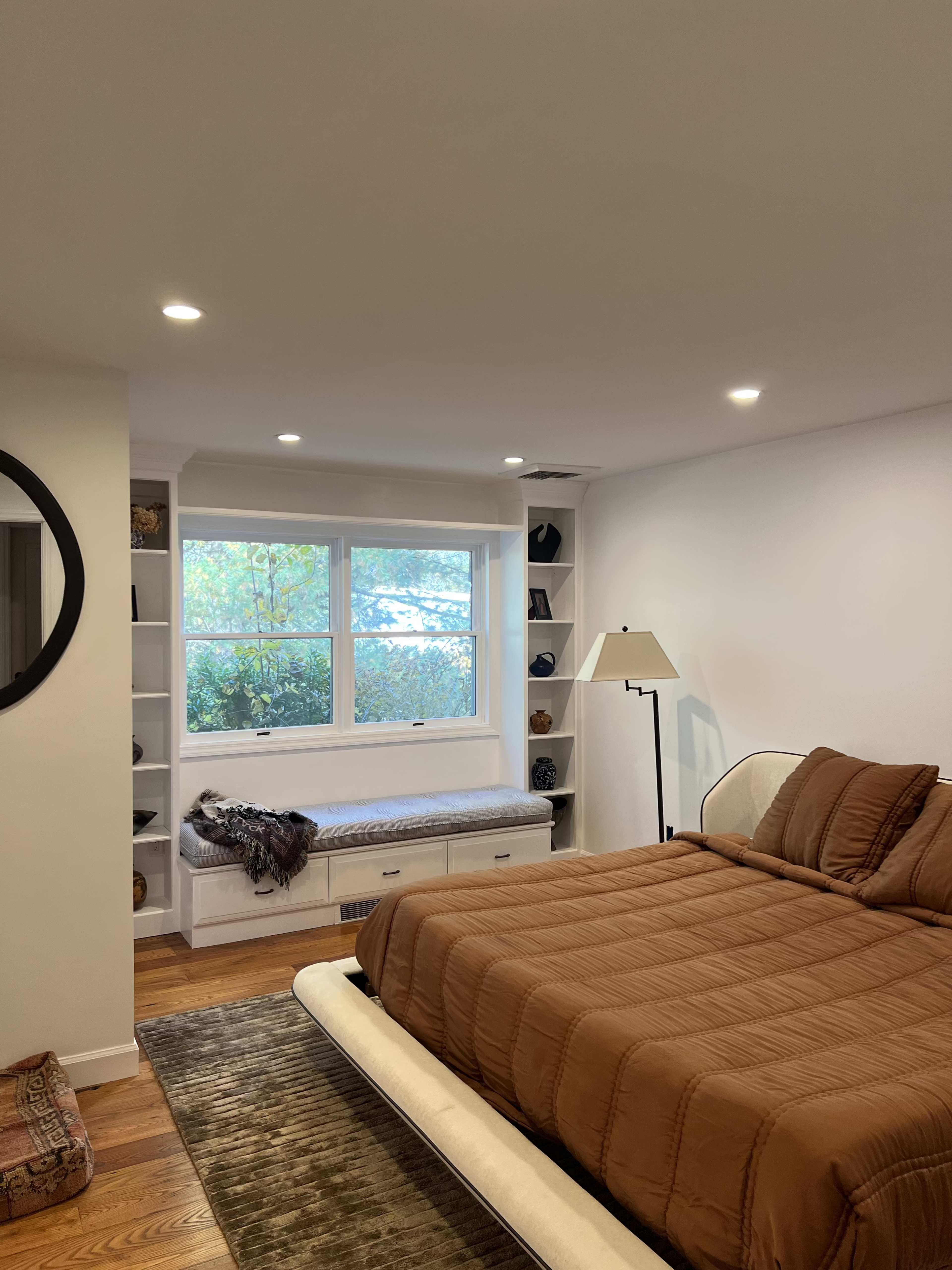 A modern bedroom featuring a bed with brown bedding, a window seat, and built-in shelves beside a large window.