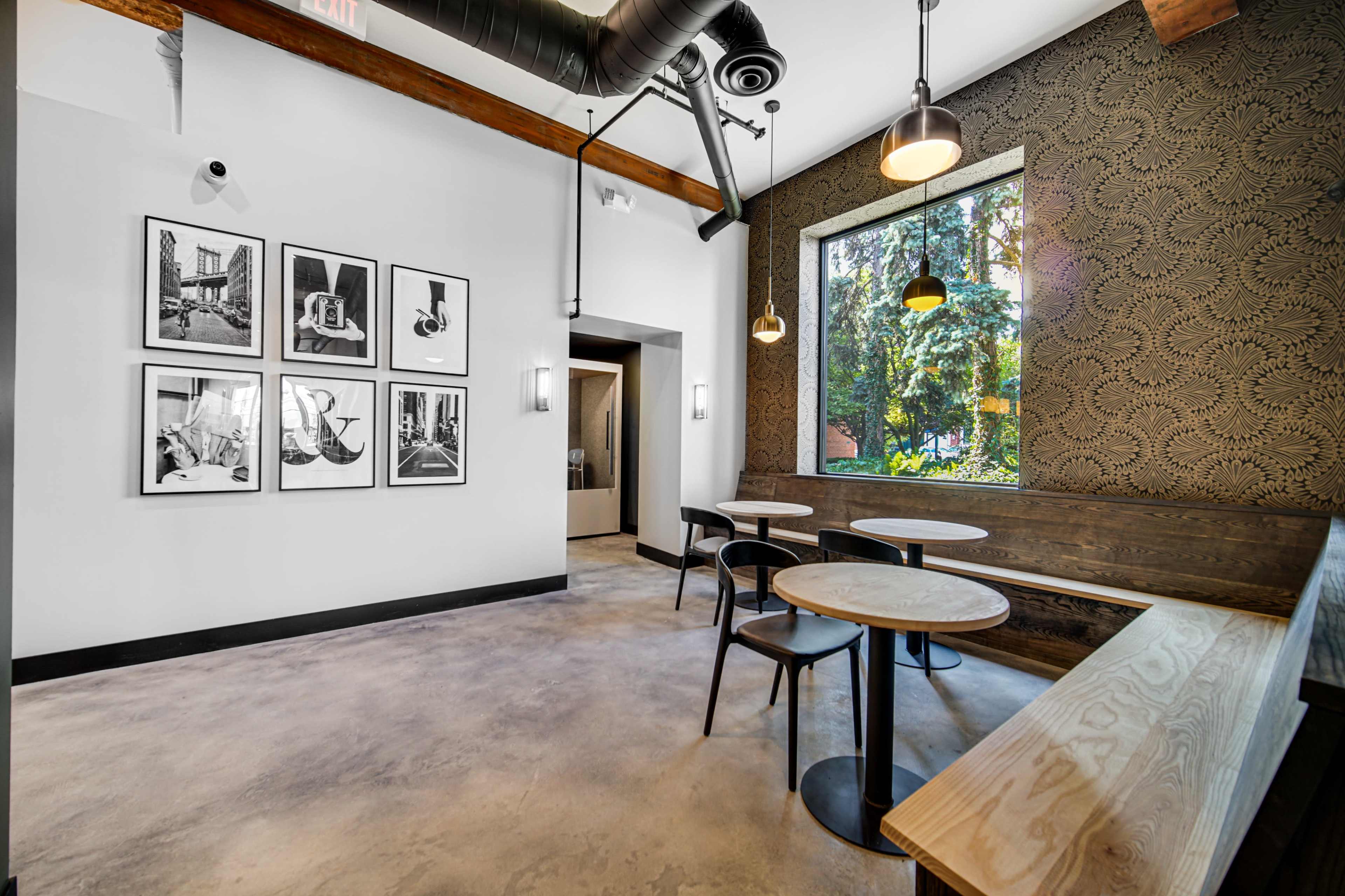 A modern cafe interior with black and white framed photos on the wall, wooden seating, and large windows overlooking greenery.