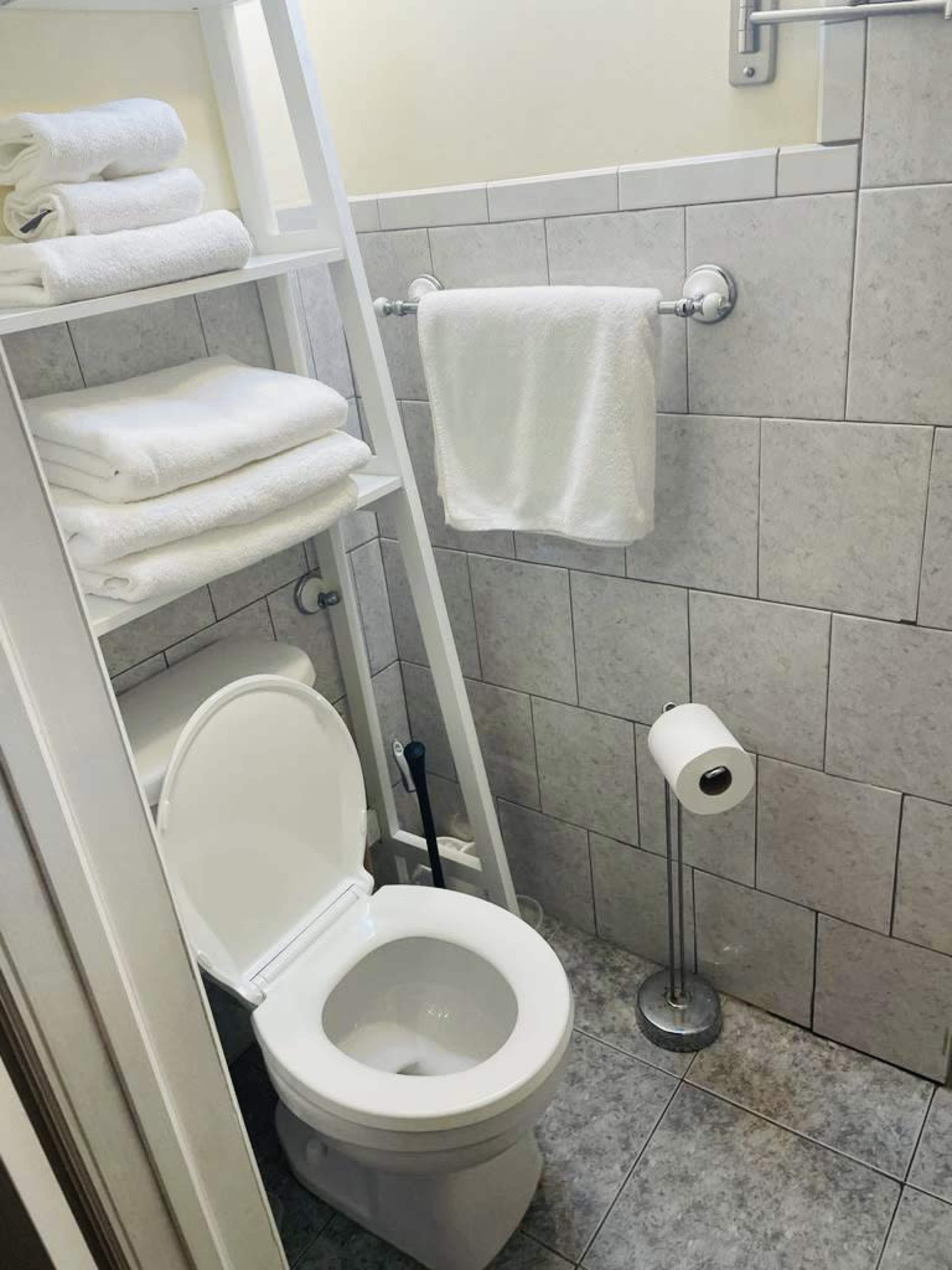 A small bathroom with a toilet, a towel rack, and stacked towels on a shelf.