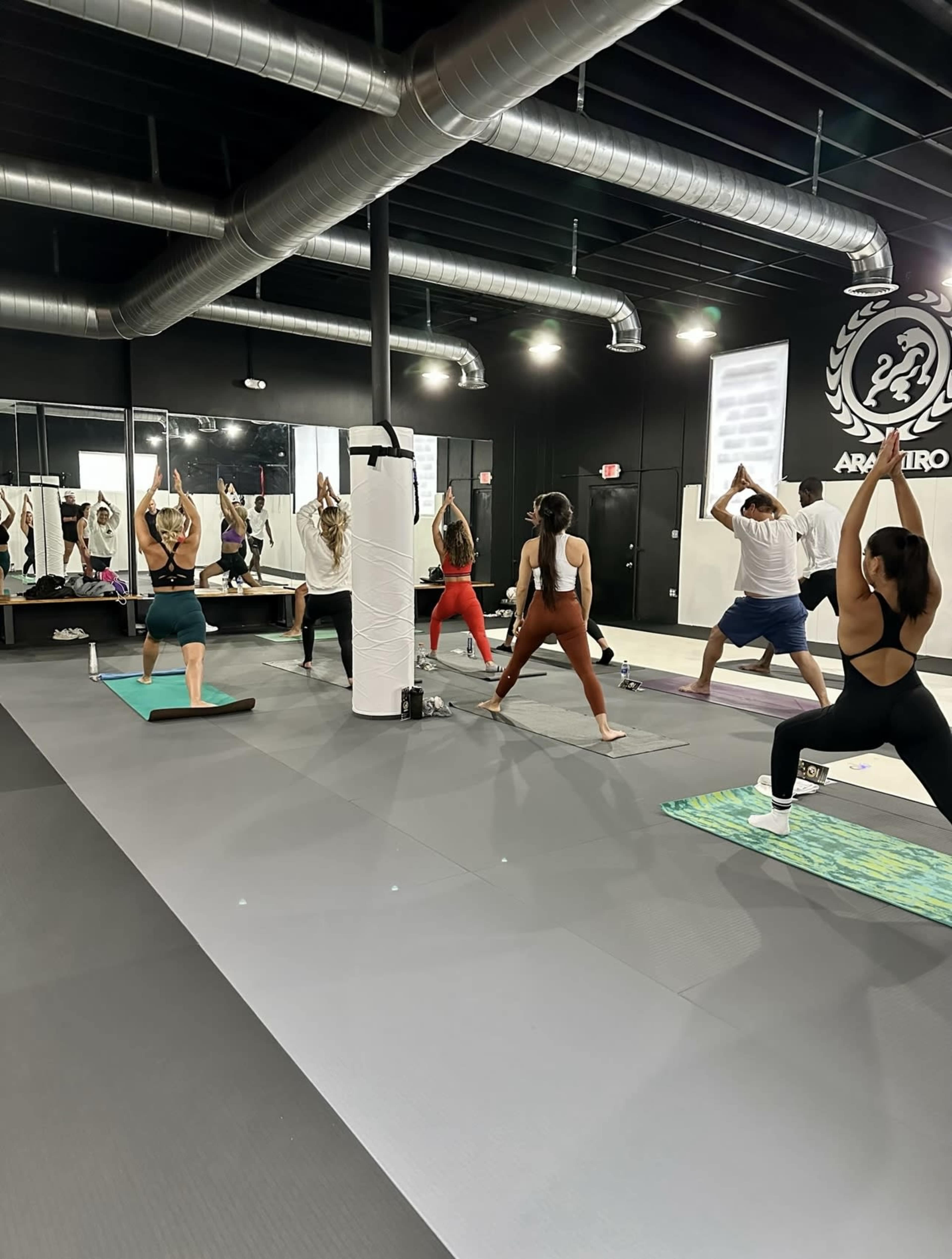 A group of individuals practices yoga in a modern fitness studio with mirrored walls and wooden flooring.