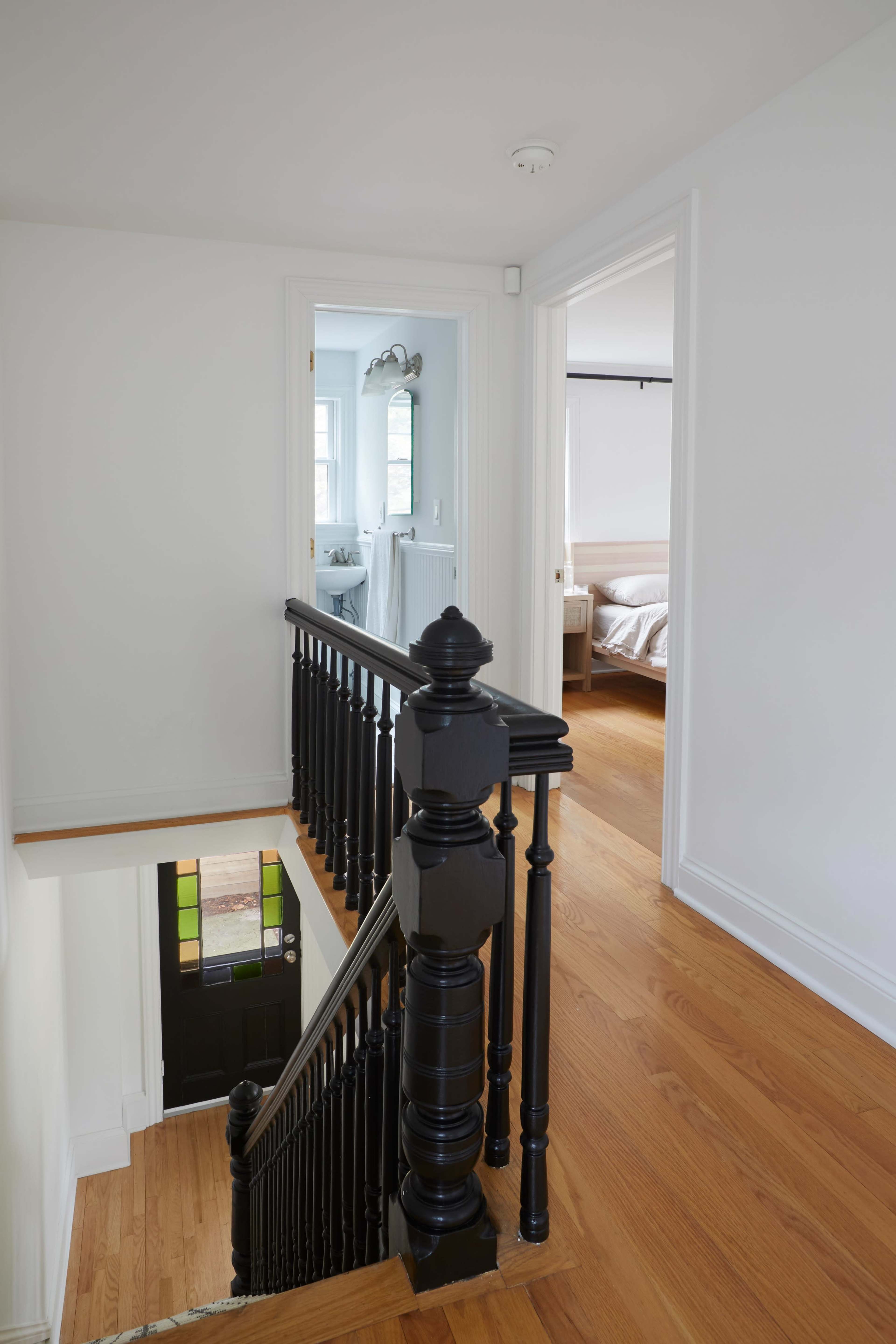 A hallway with a wooden staircase leads to a door at the bottom, while an open doorway reveals a bedroom and a bathroom at the top.
