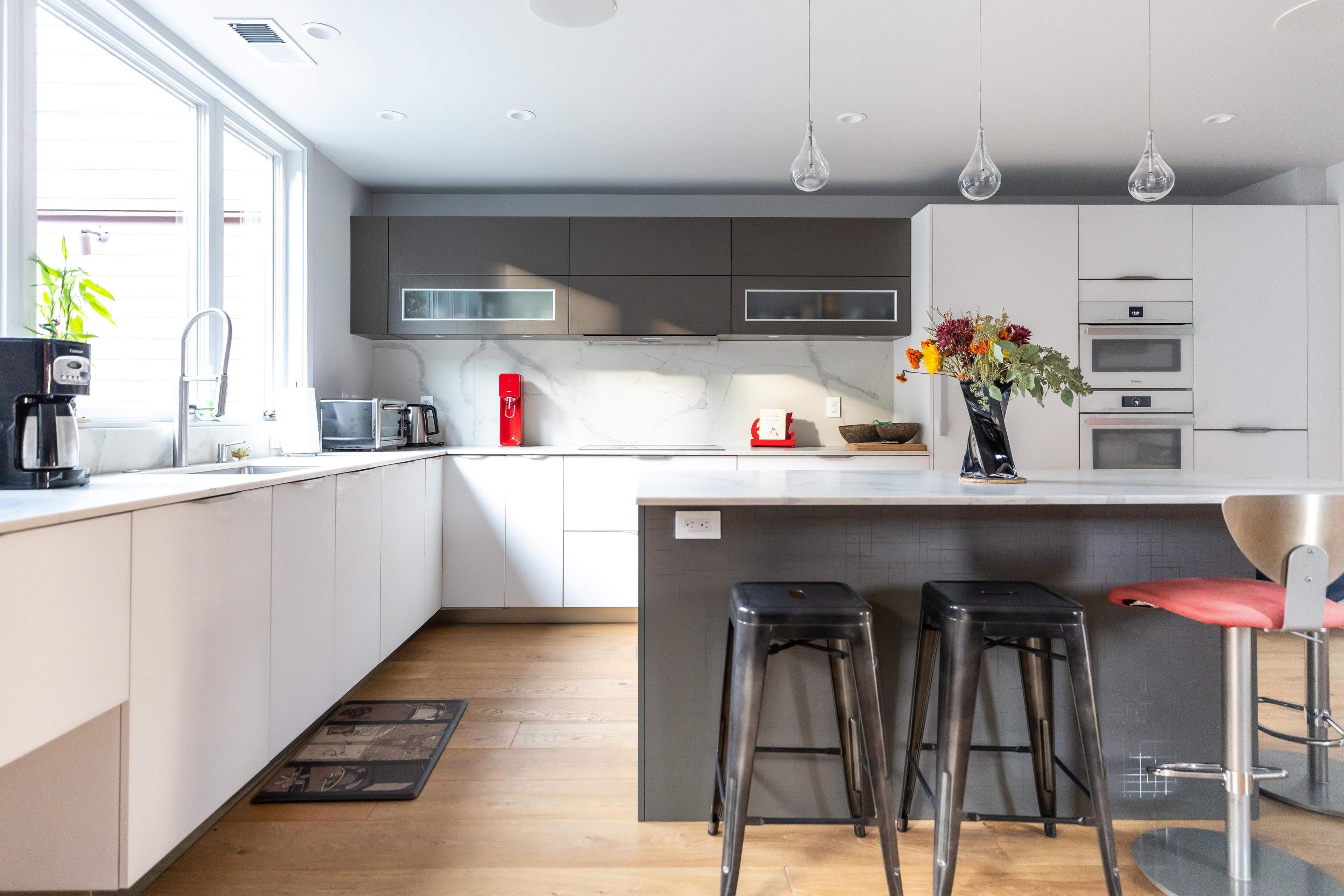 A modern kitchen with white and gray cabinetry, stainless steel appliances, and a central island with bar stools.