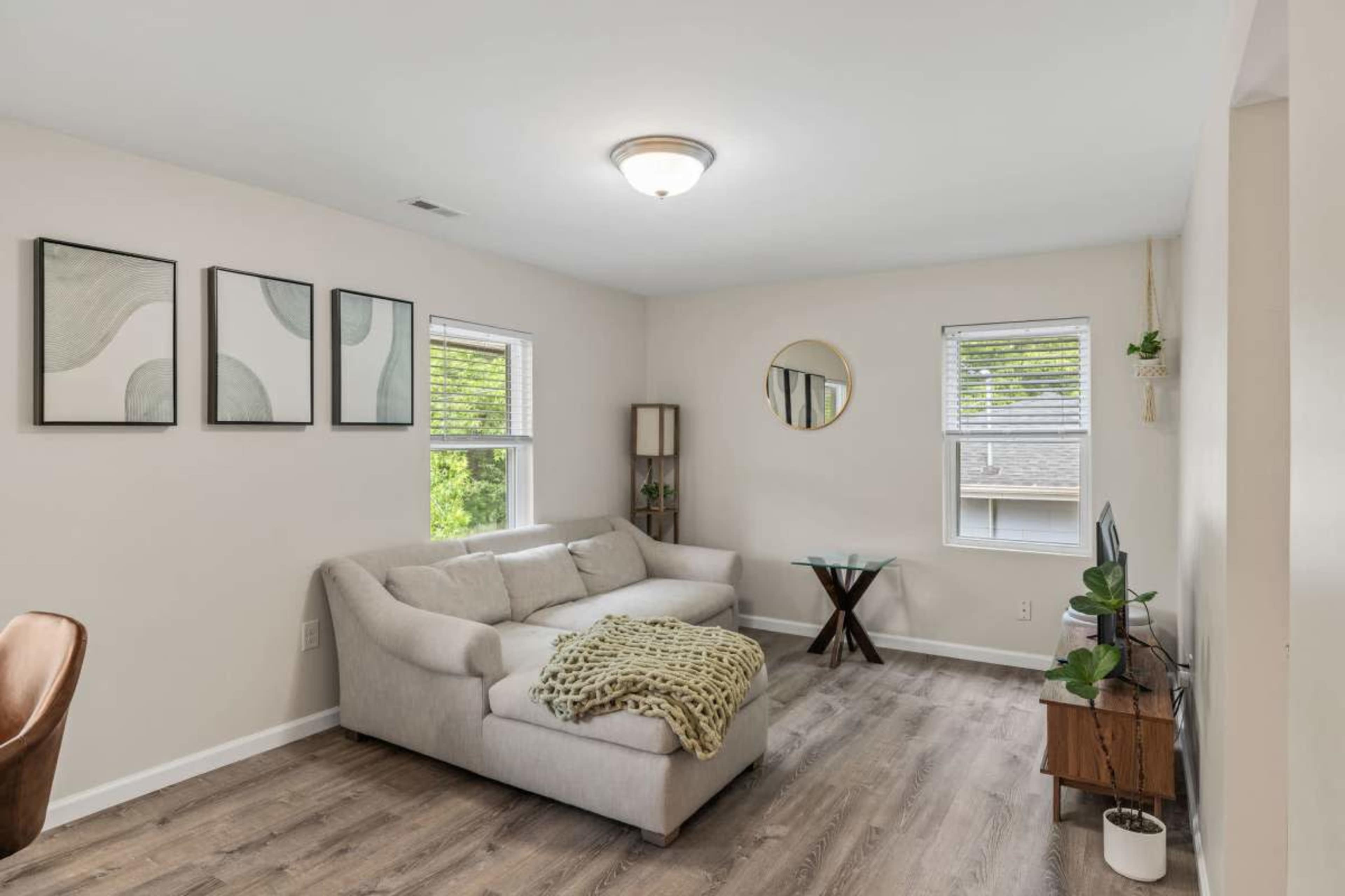 The image shows a living room with a light-colored sofa, a small round mirror on the wall, and a green plant displayed on a side table.