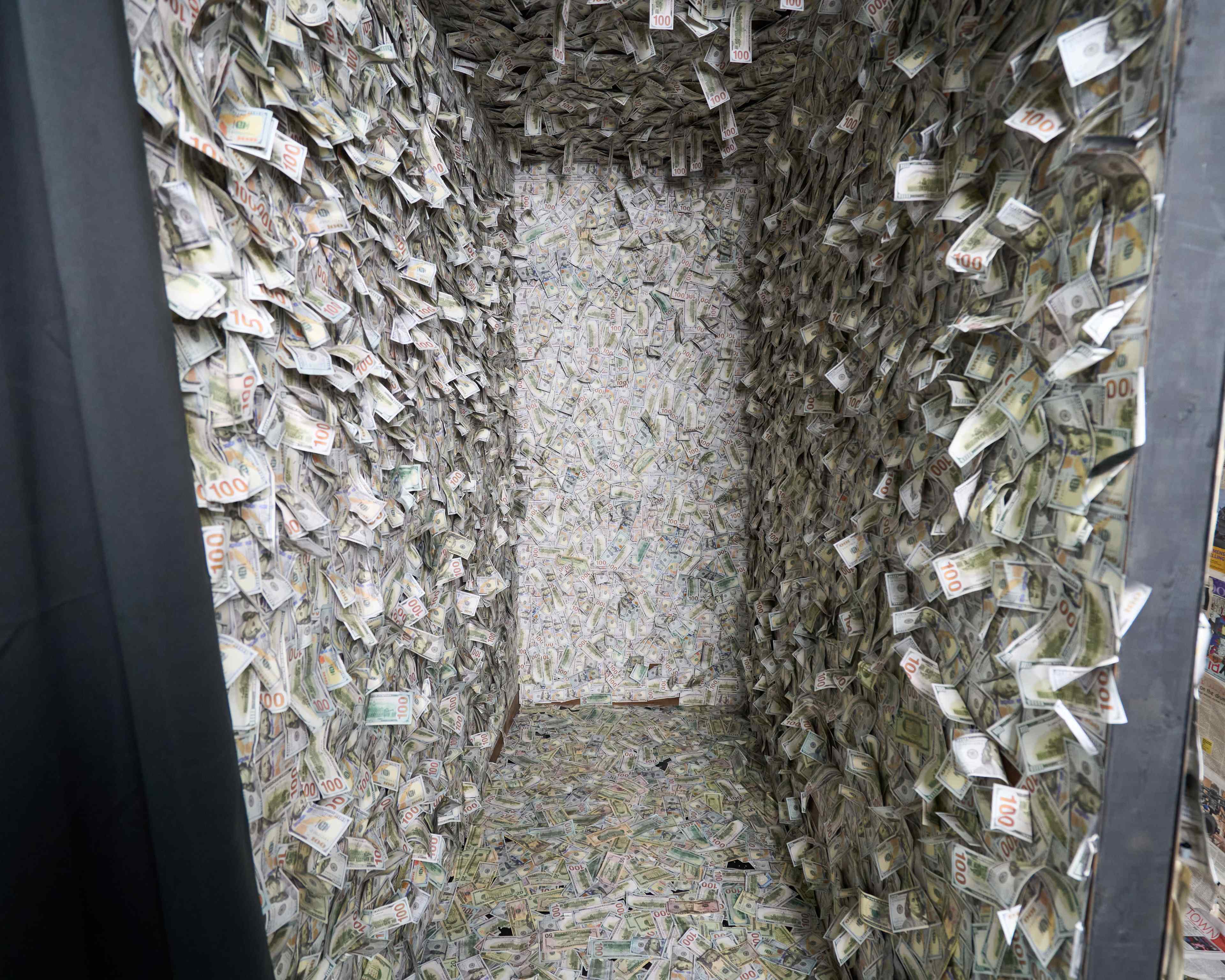 The image shows a small room completely filled with crumpled dollar bills stuck to the walls and floor.