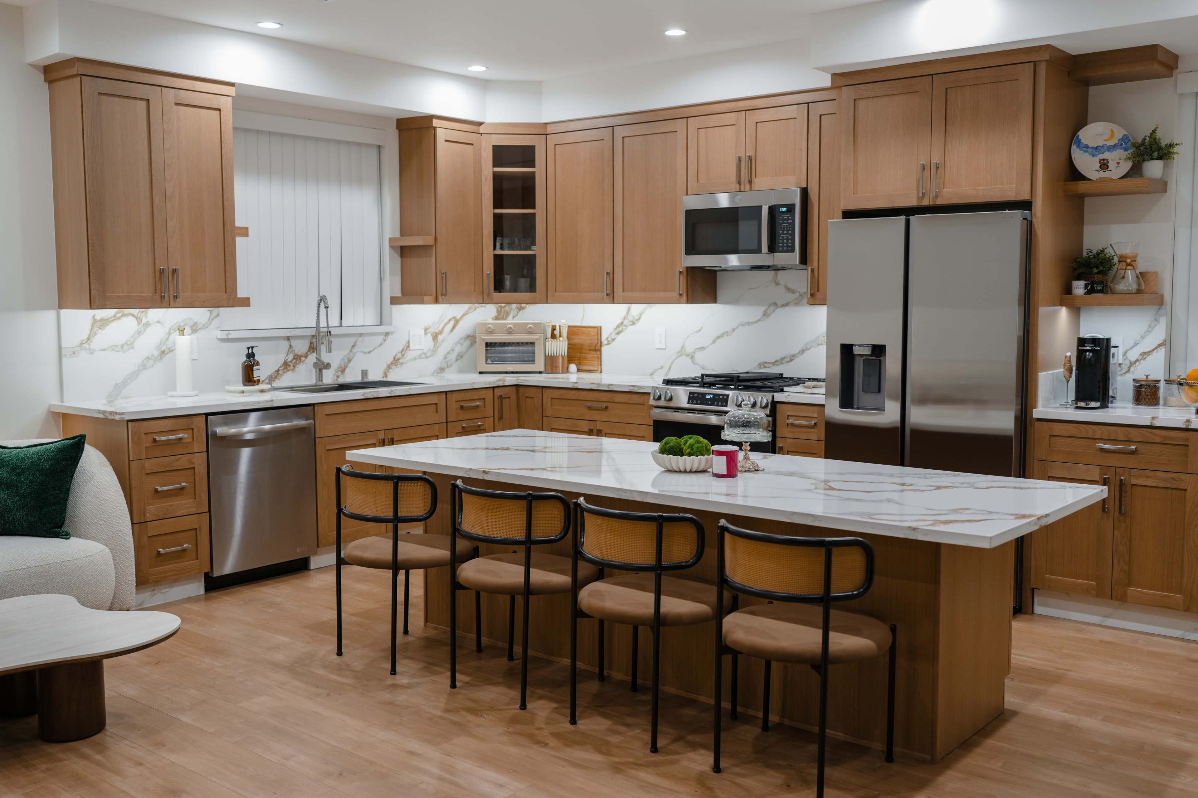 The kitchen features wooden cabinetry, stainless steel appliances, and a large marble-topped island with seating.