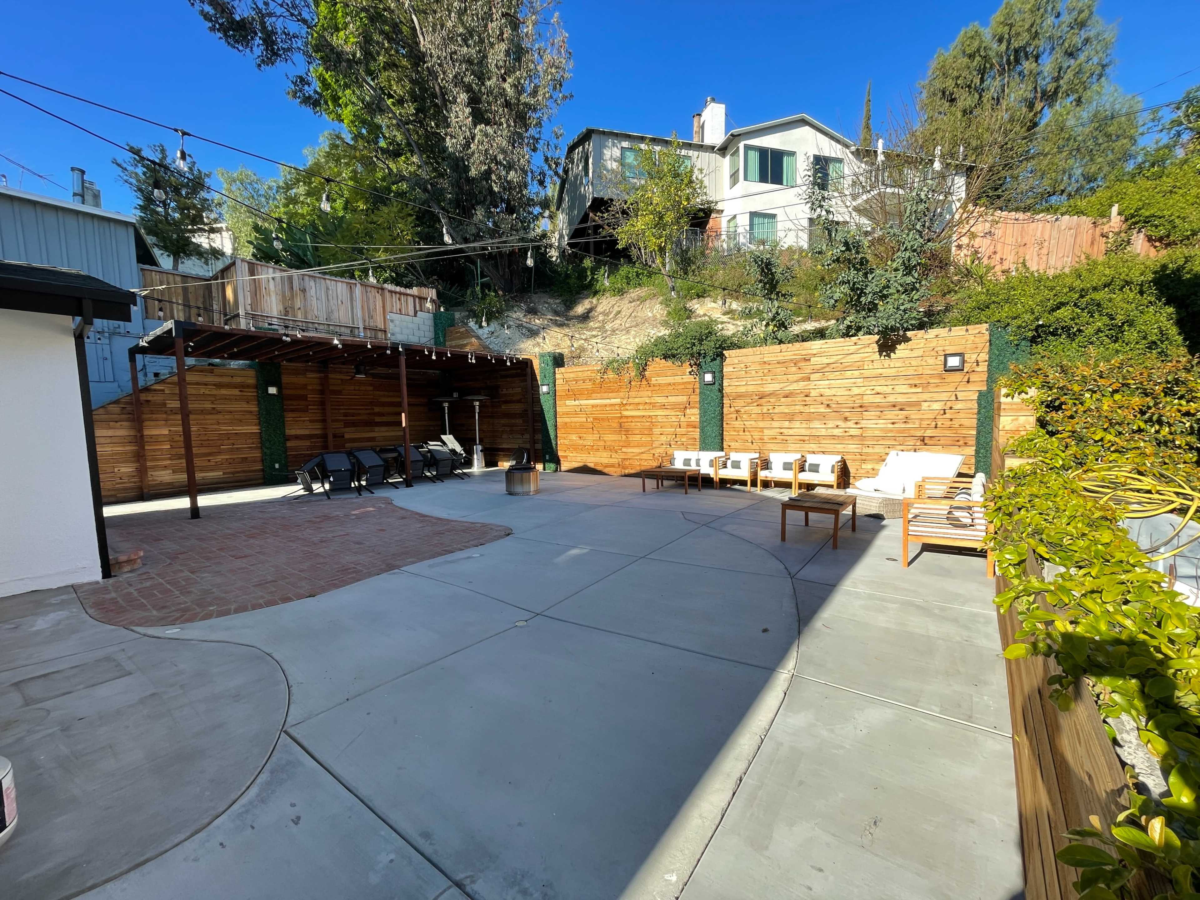 A landscaped outdoor patio area with a brick path, seating, and wooden fencing surrounded by greenery.