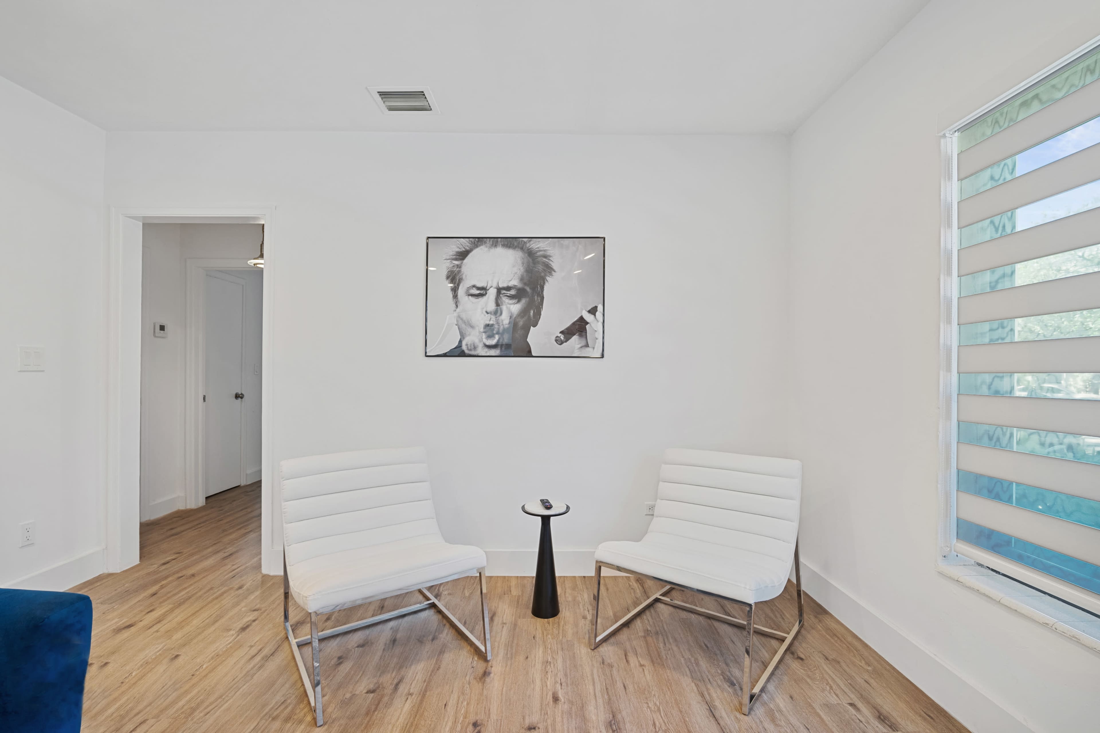 The image shows two white chairs facing each other in a bright room with a black vase and a framed artwork on the wall.