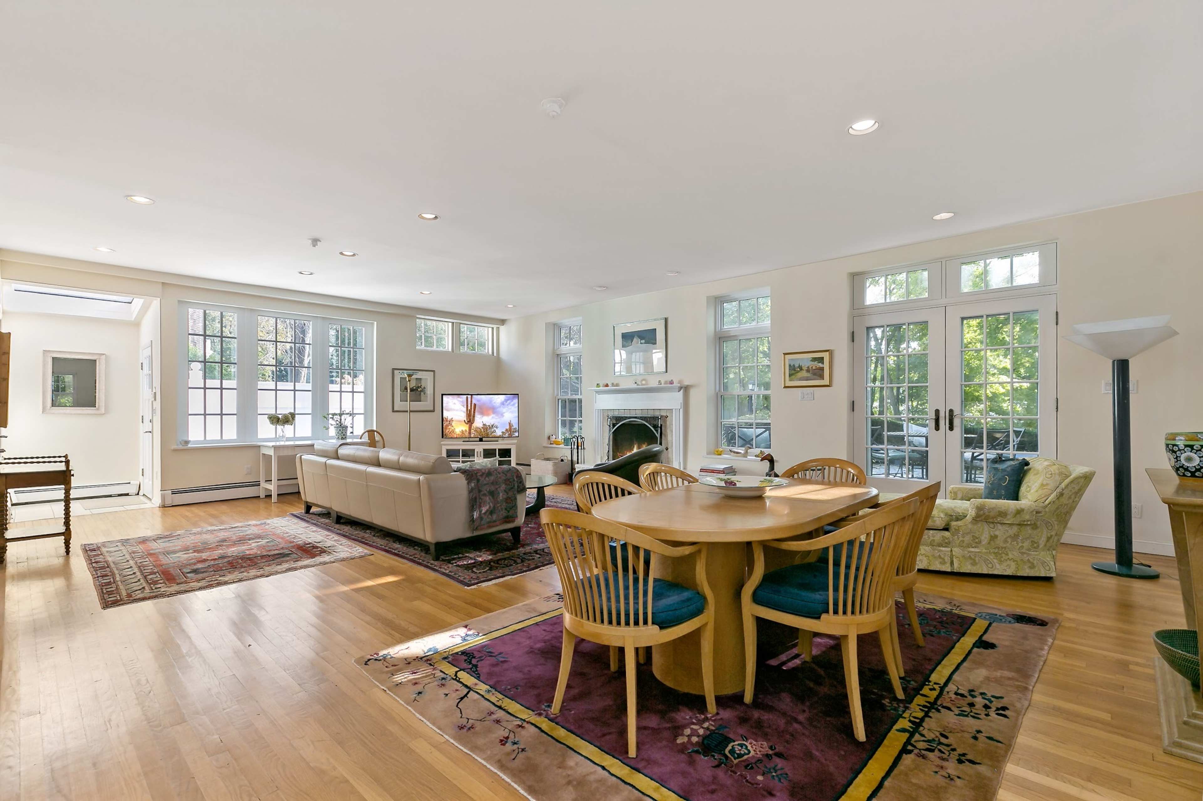 A spacious living area with a dining table, a couch, a television, and large windows that provide natural light.