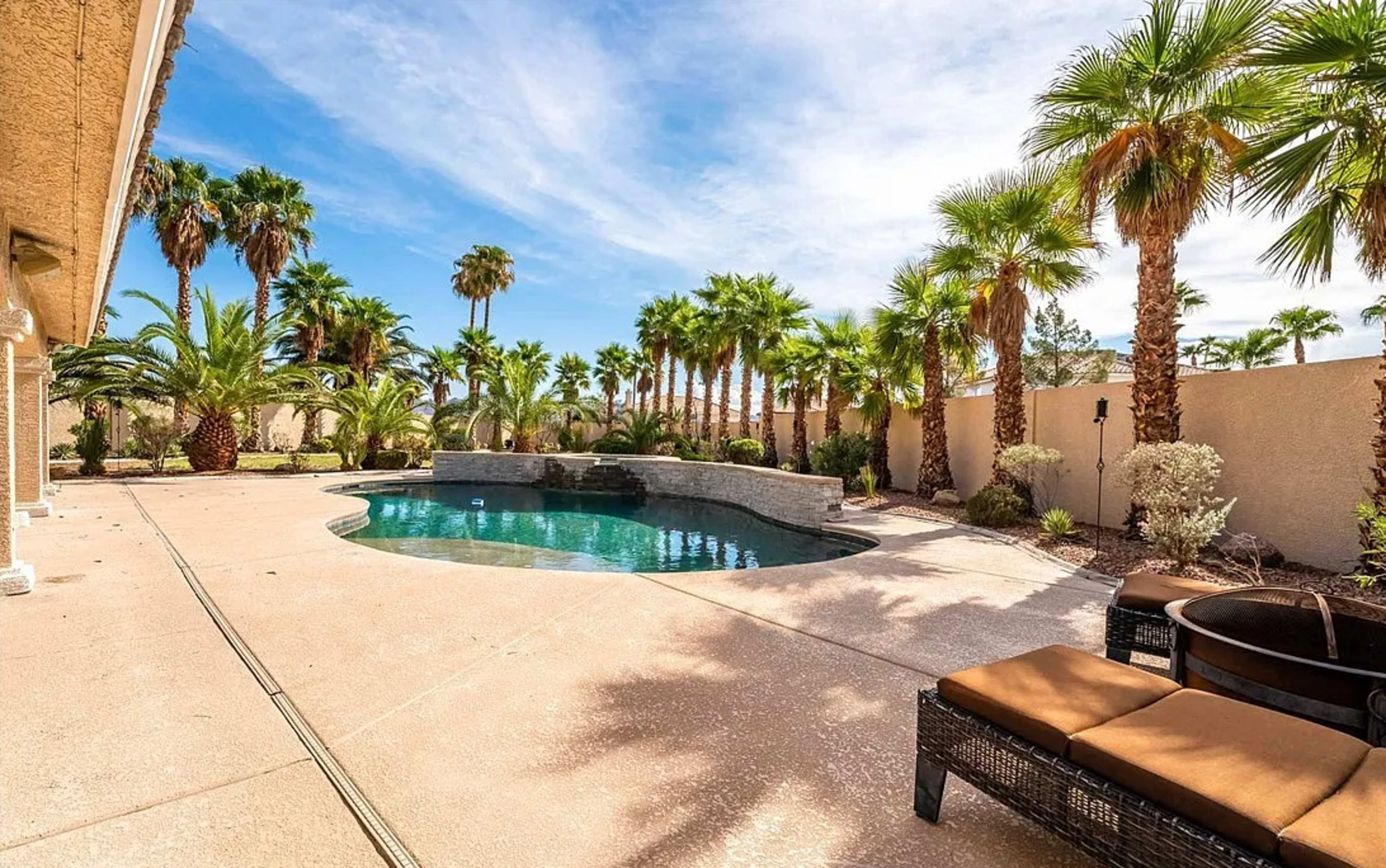 The image shows a sunny outdoor space featuring a swimming pool surrounded by palm trees and outdoor furniture.