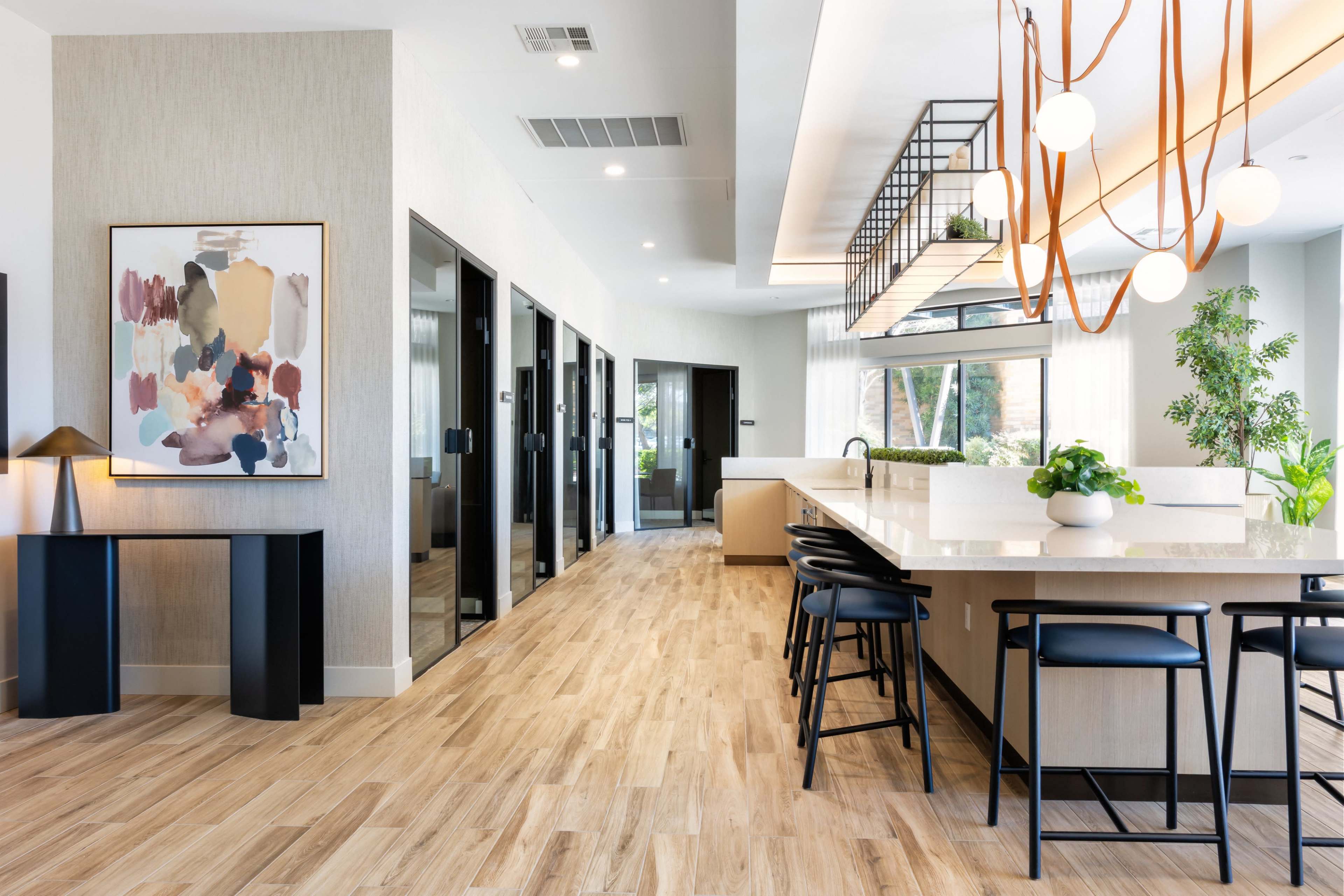 The image shows a modern kitchen and dining area with a long island, black bar stools, and large windows allowing natural light to fill the space.
