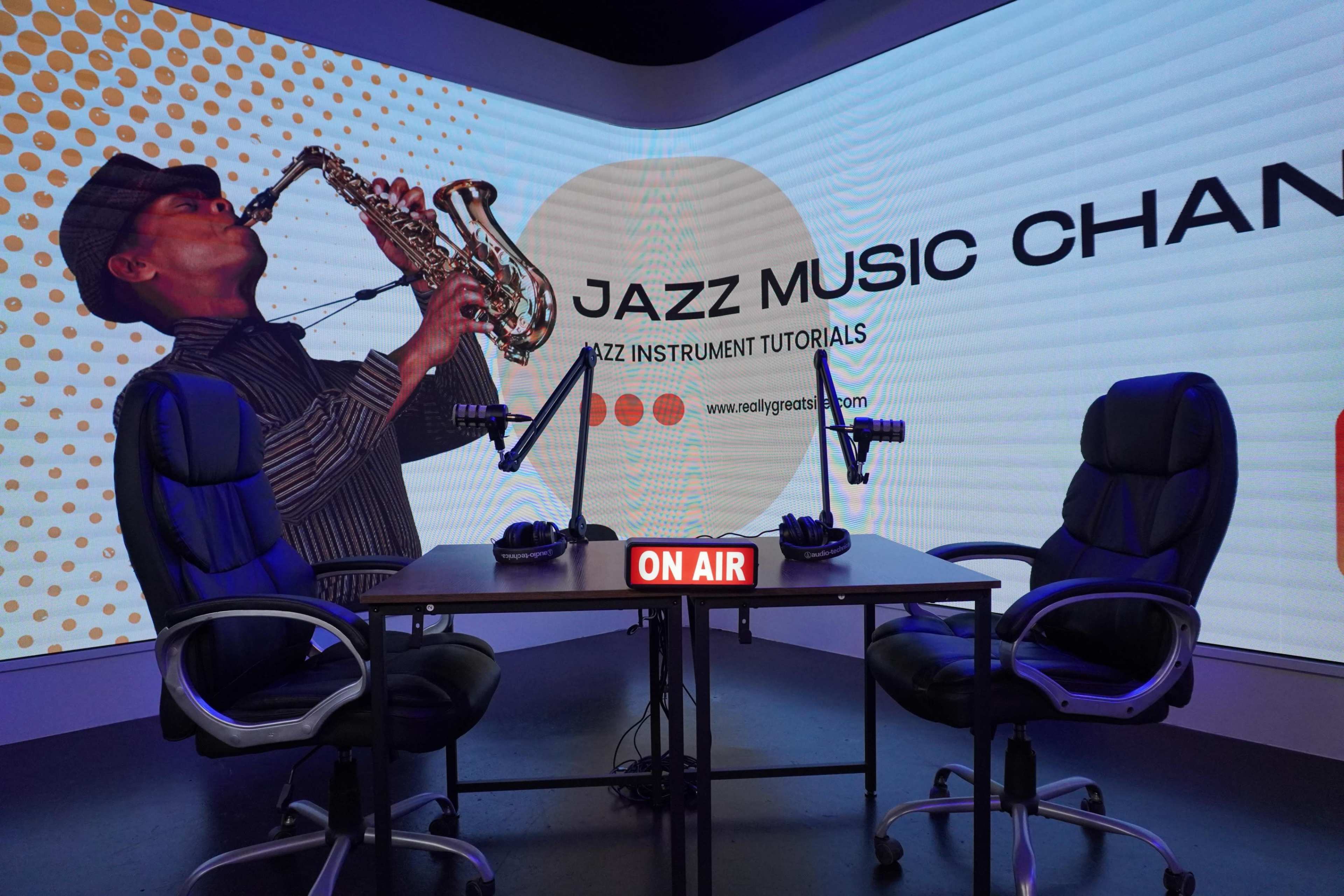 The image shows a modern studio setup for a jazz music channel, featuring a table with two black chairs, microphones, and a large screen displaying a musician playing saxophone.
