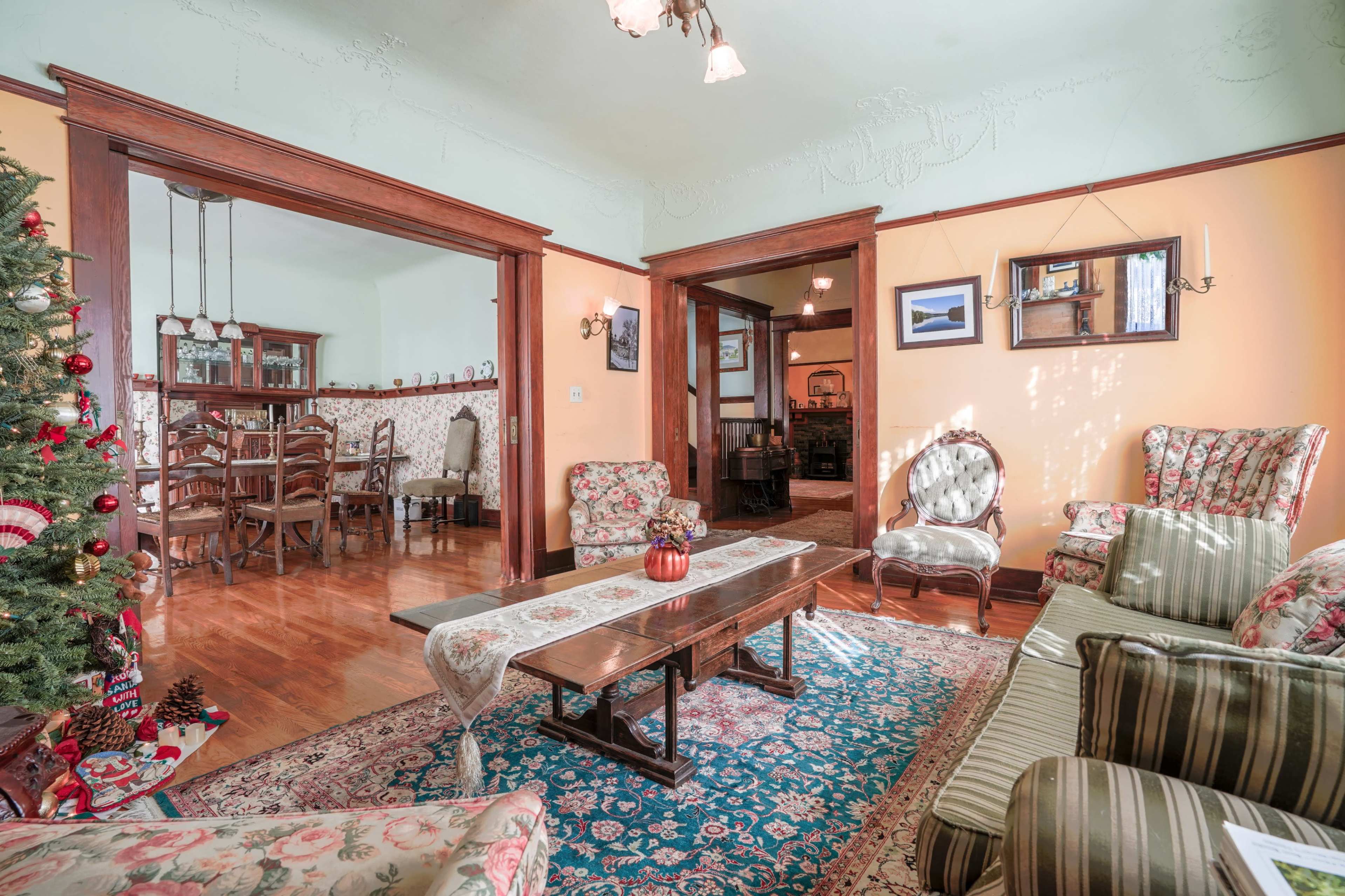 The living room features floral-patterned furniture, a wooden coffee table, and a Christmas tree, with clear sightlines to a dining area in the background.