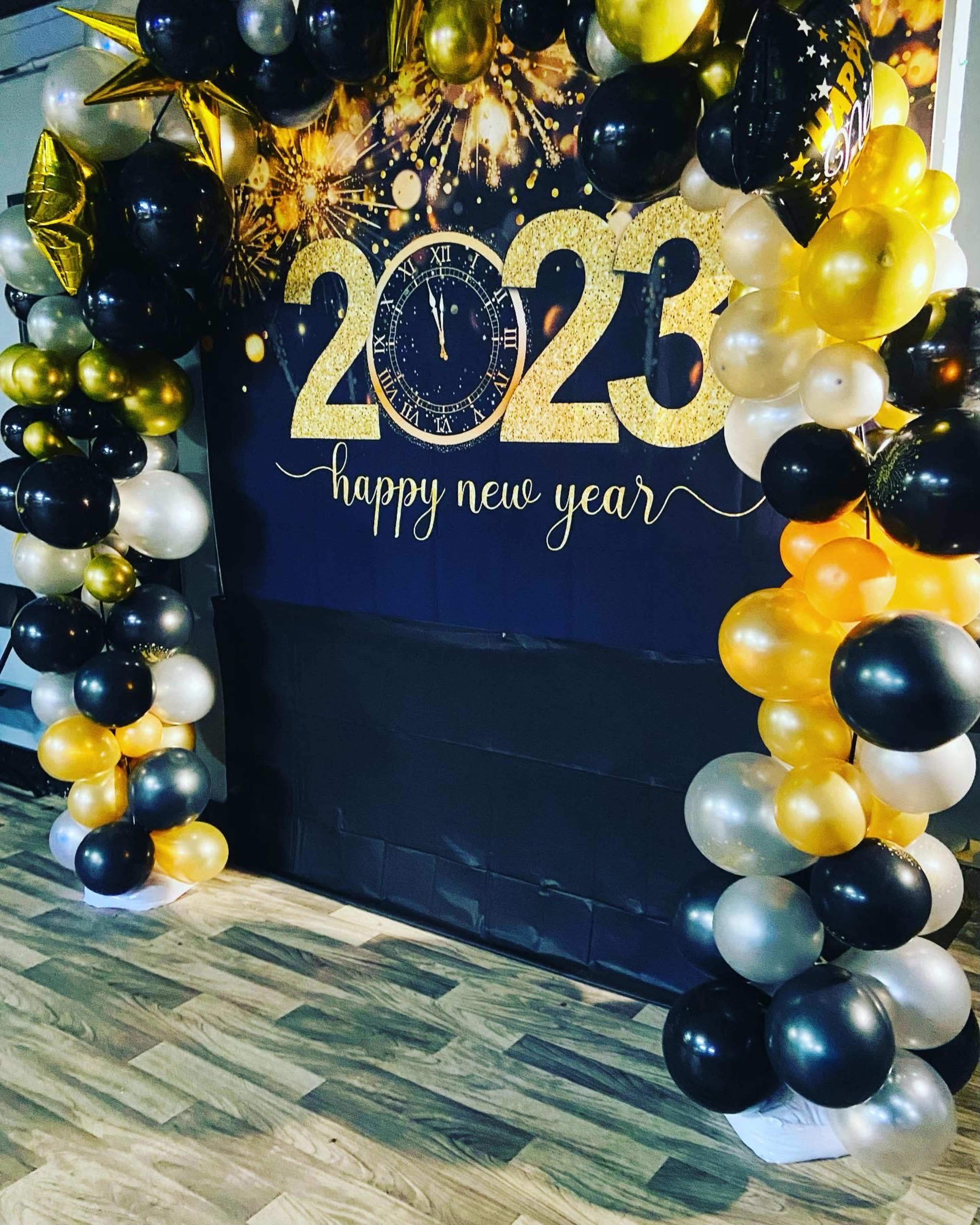 The image features a decorative archway made of black, gold, and white balloons, with a "2023 Happy New Year" banner and a clock graphic.