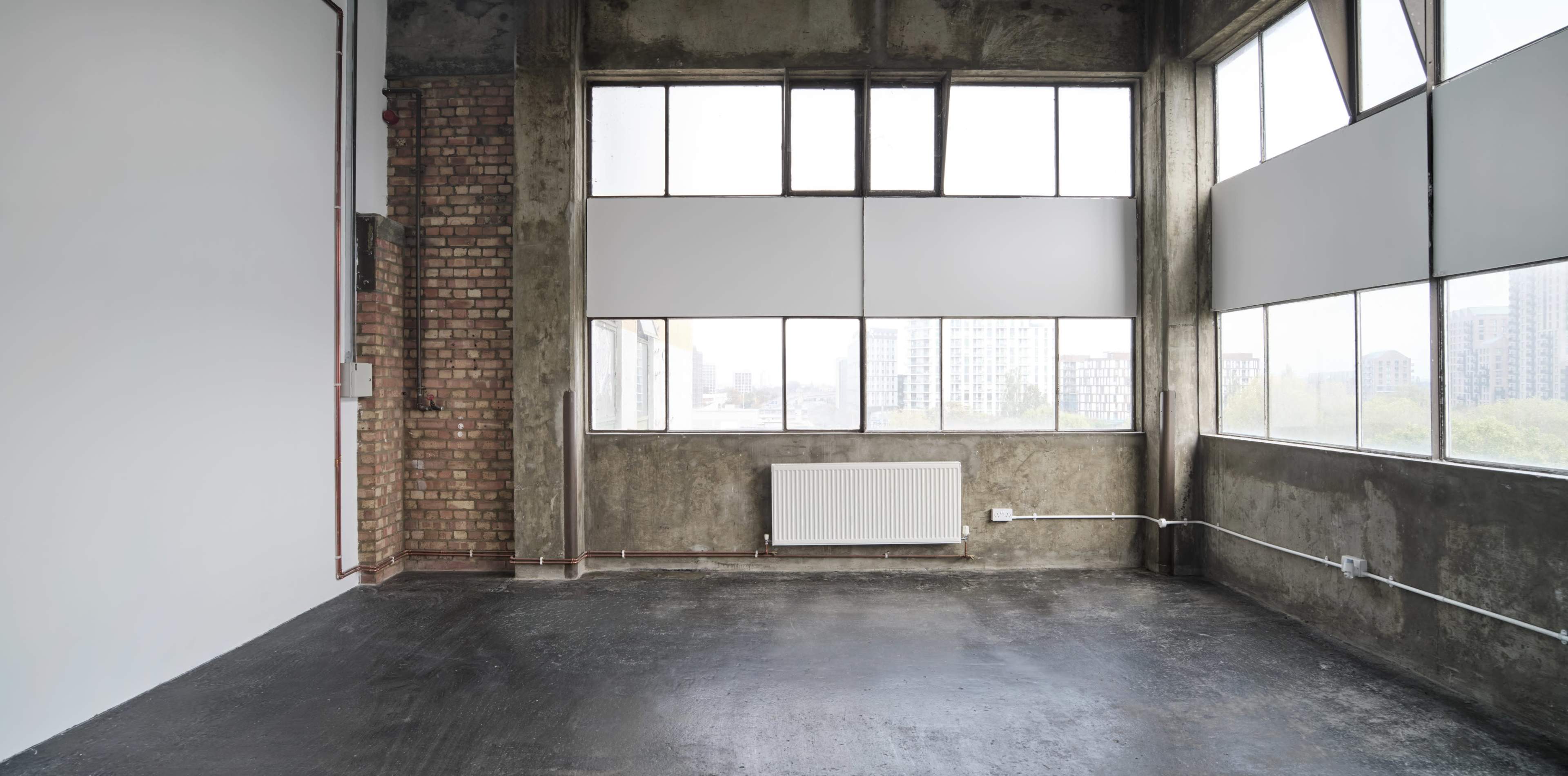 The image shows a spacious industrial-style room with large windows, exposed brick walls, and a polished concrete floor.
