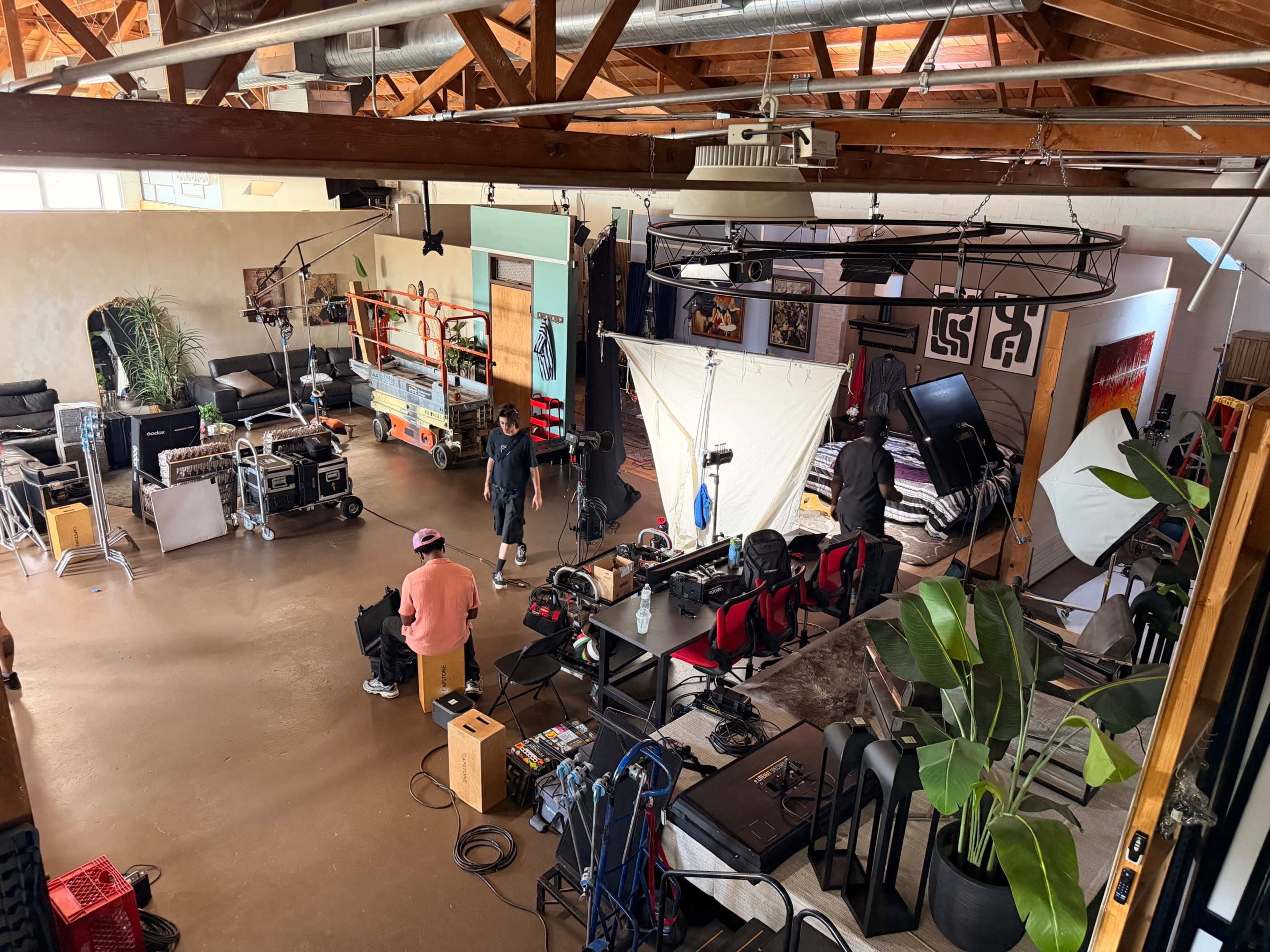 The image shows a spacious studio or creative workspace with equipment, seating areas, and a few people preparing for a shoot.