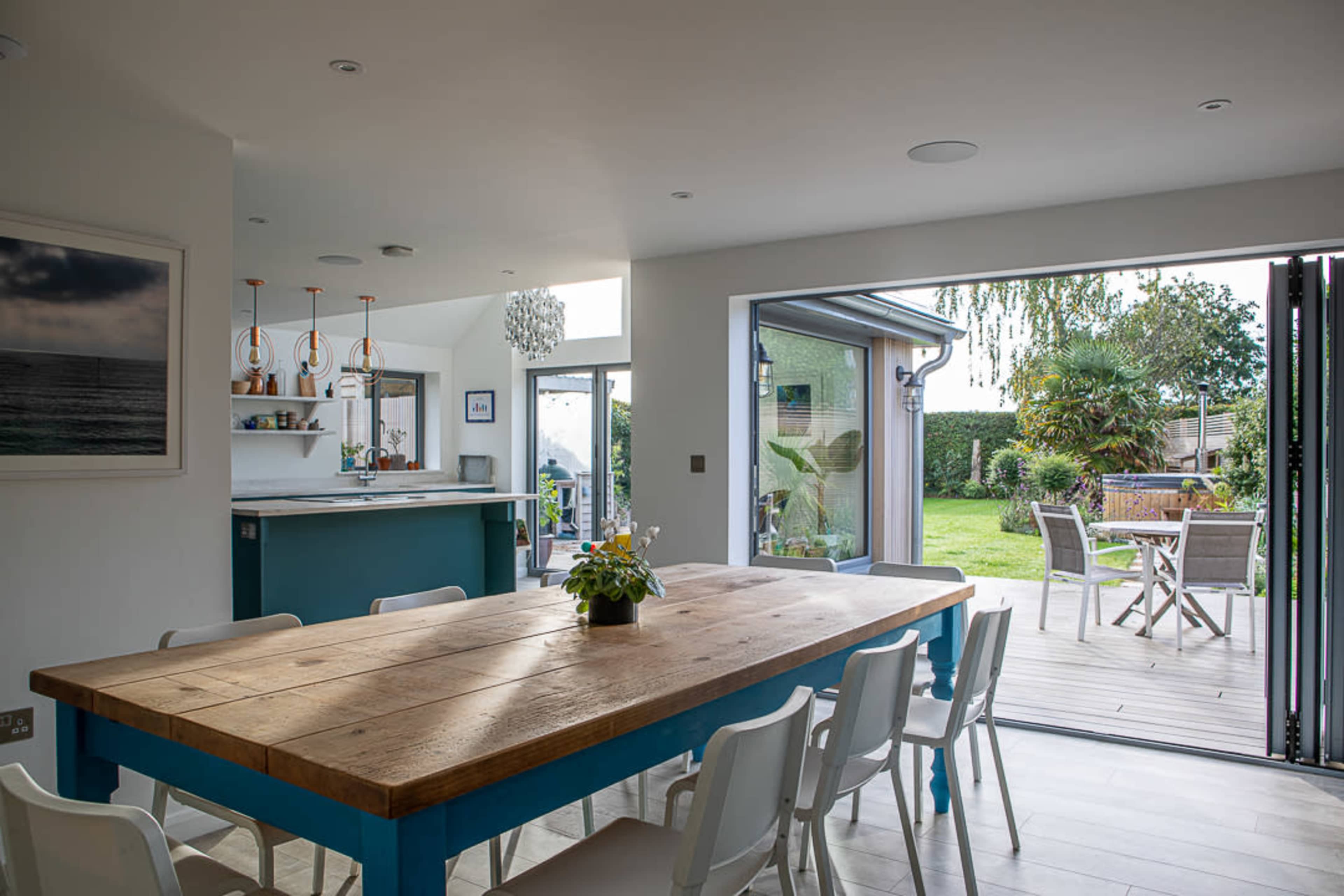 A spacious dining area features a large wooden table surrounded by white chairs, with a view of a backyard through glass doors.