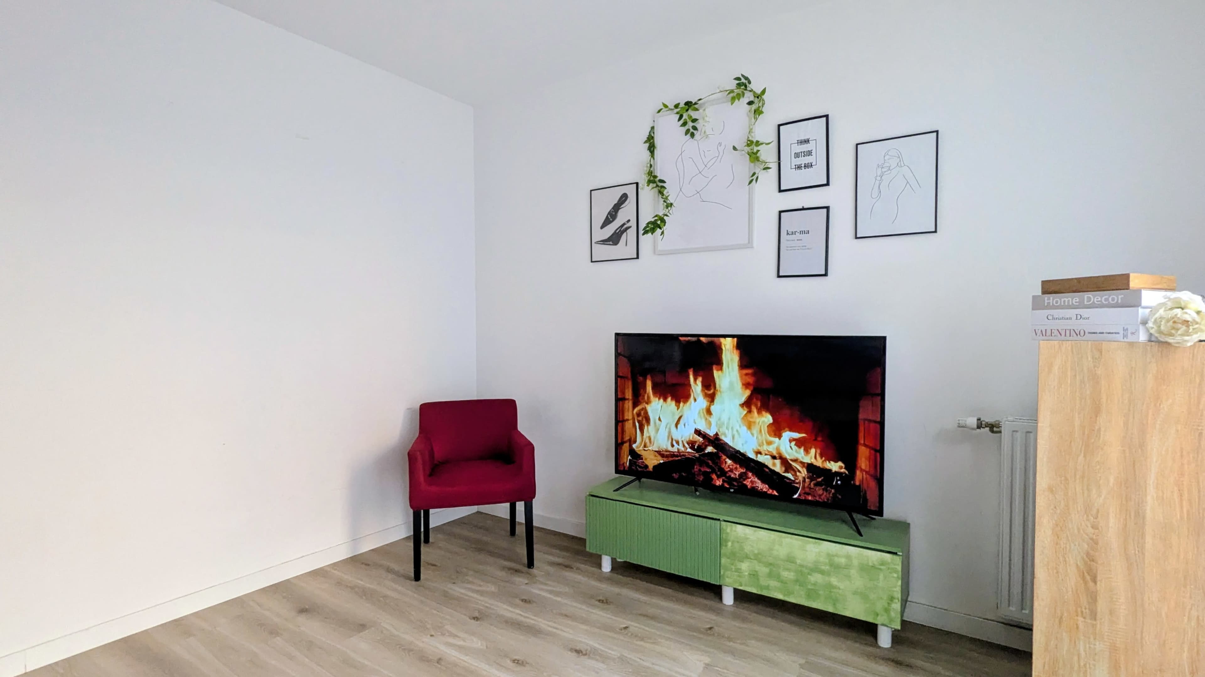 A modern living room features a green TV stand with a flat-screen television displaying a fireplace, a purple chair, and framed artwork on the white walls.
