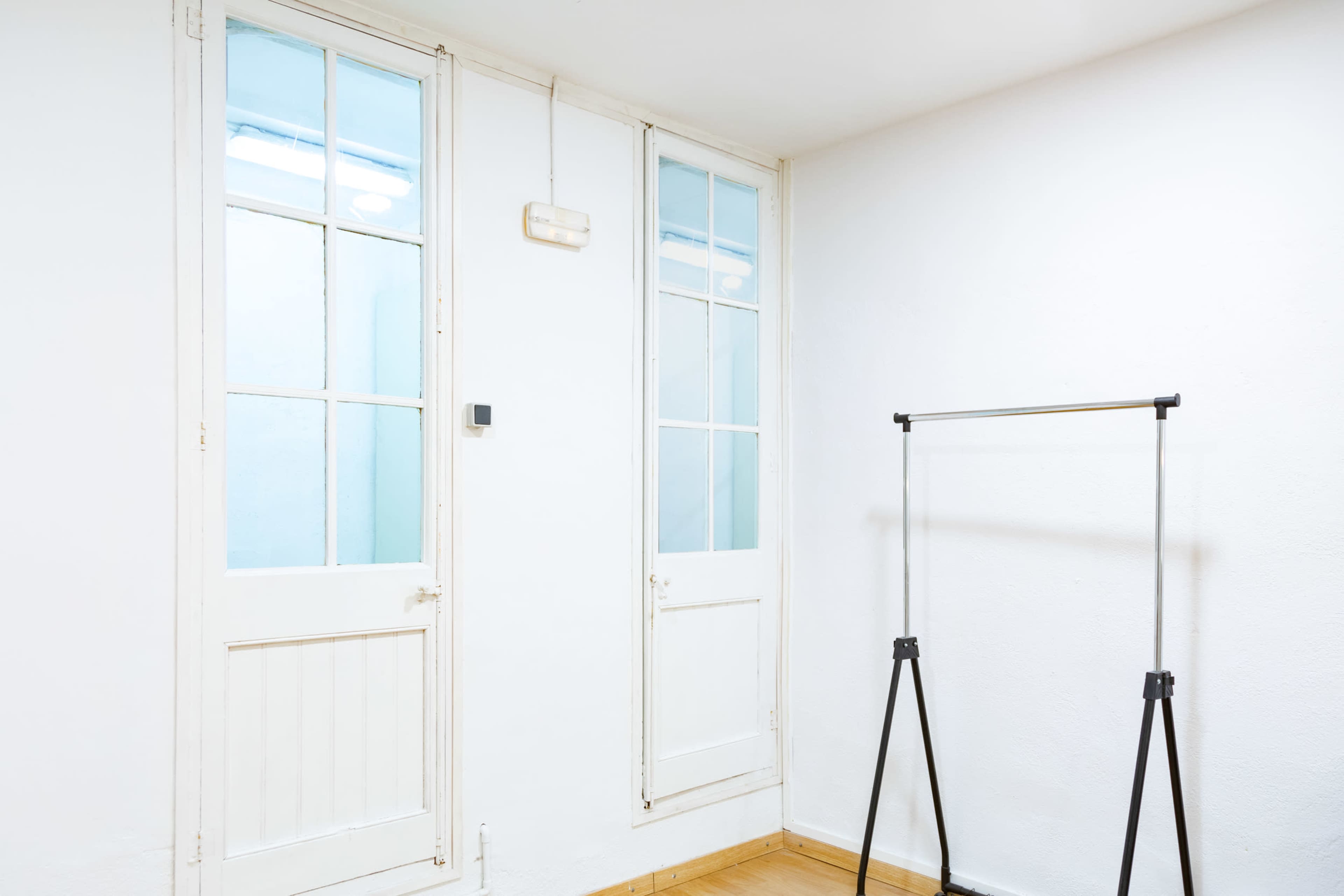 A bright interior space with two doors and a clothing rack against a white wall.