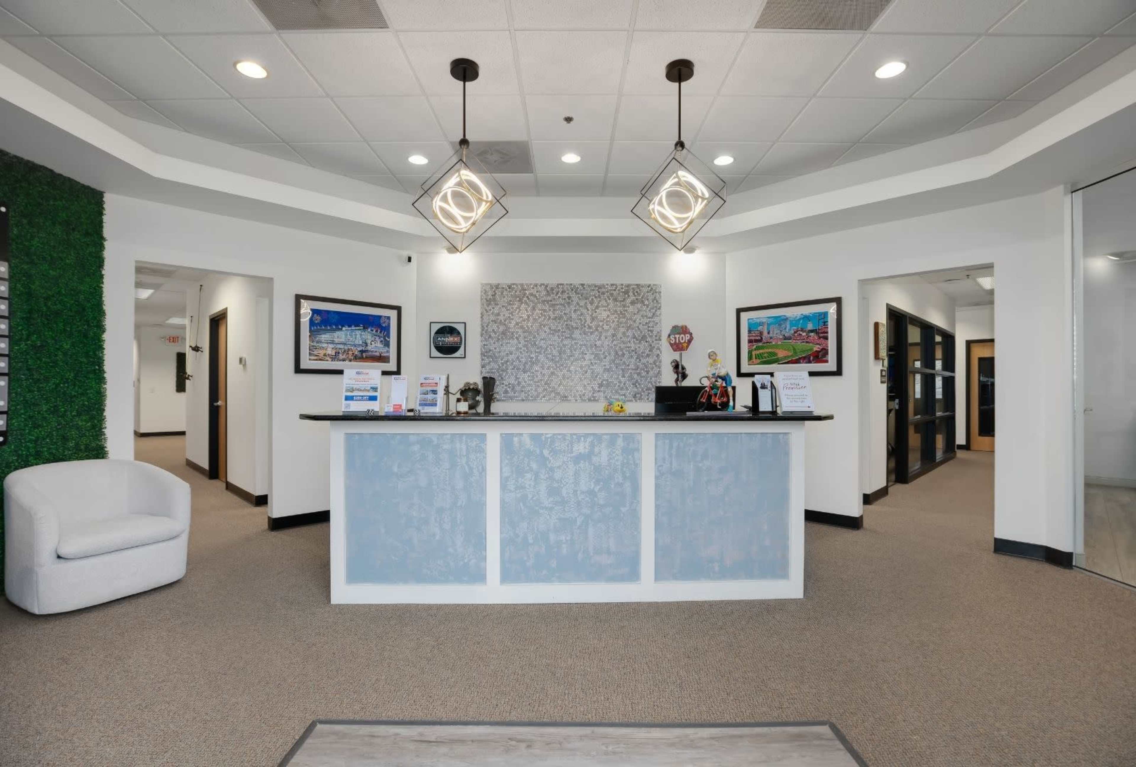 The image shows a modern reception area with a light blue front desk, two decorative light fixtures, and framed artwork on the walls.