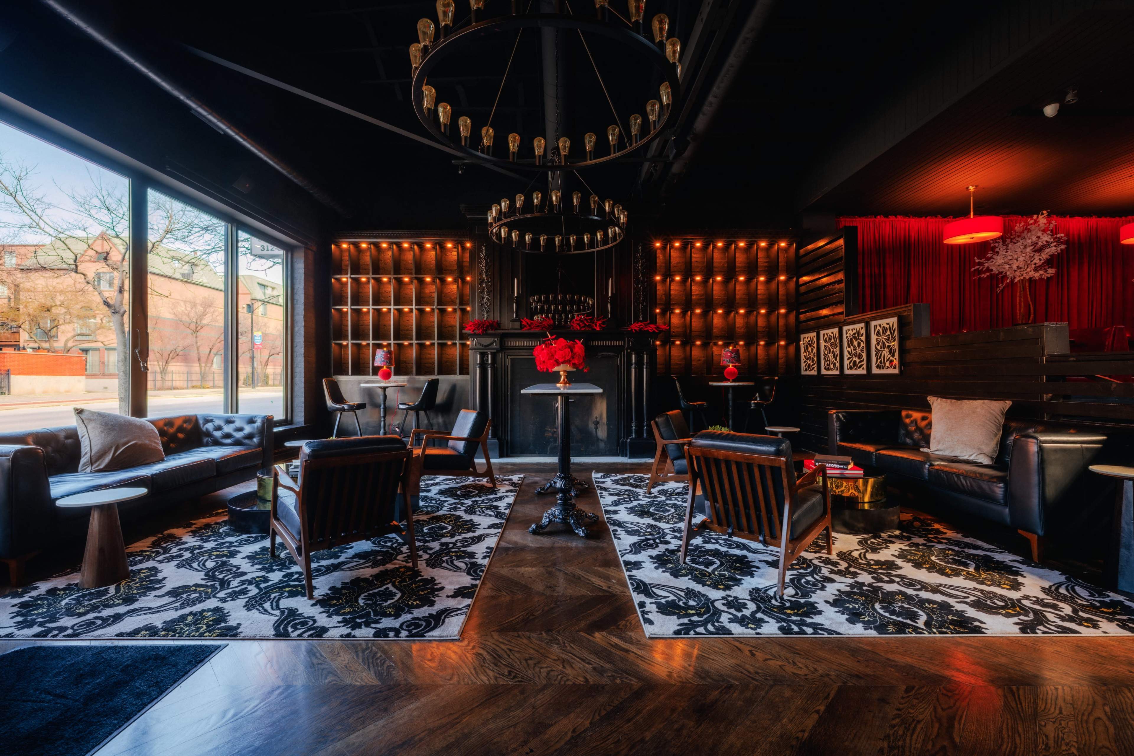 The image shows a stylish lounge with dark walls, a chandelier, and seating arranged around a central area adorned with a patterned rug.