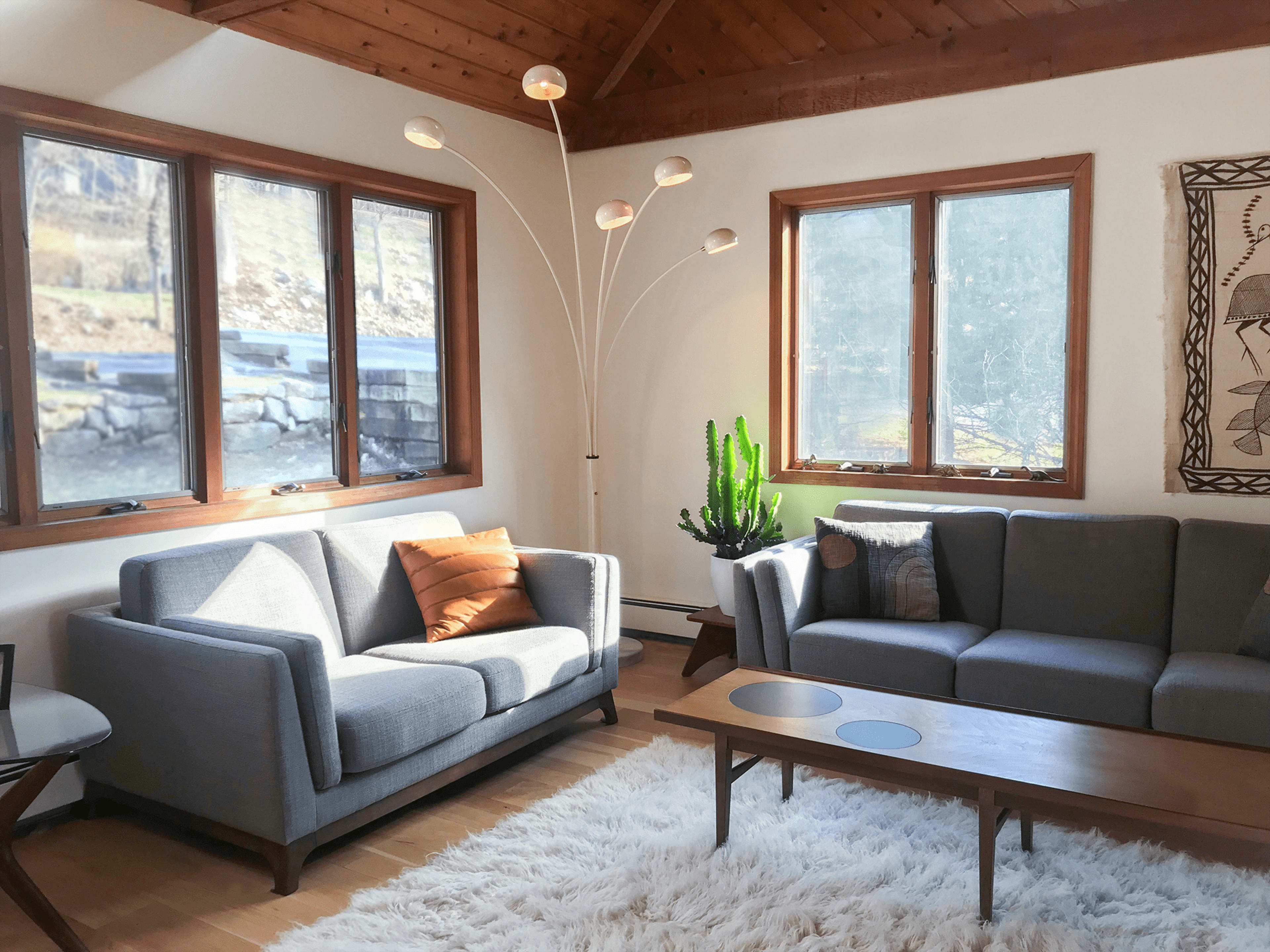 The image shows a living room with a gray sofa, a gray loveseat, a wooden coffee table, and a floor lamp, all complemented by natural light coming through large windows.