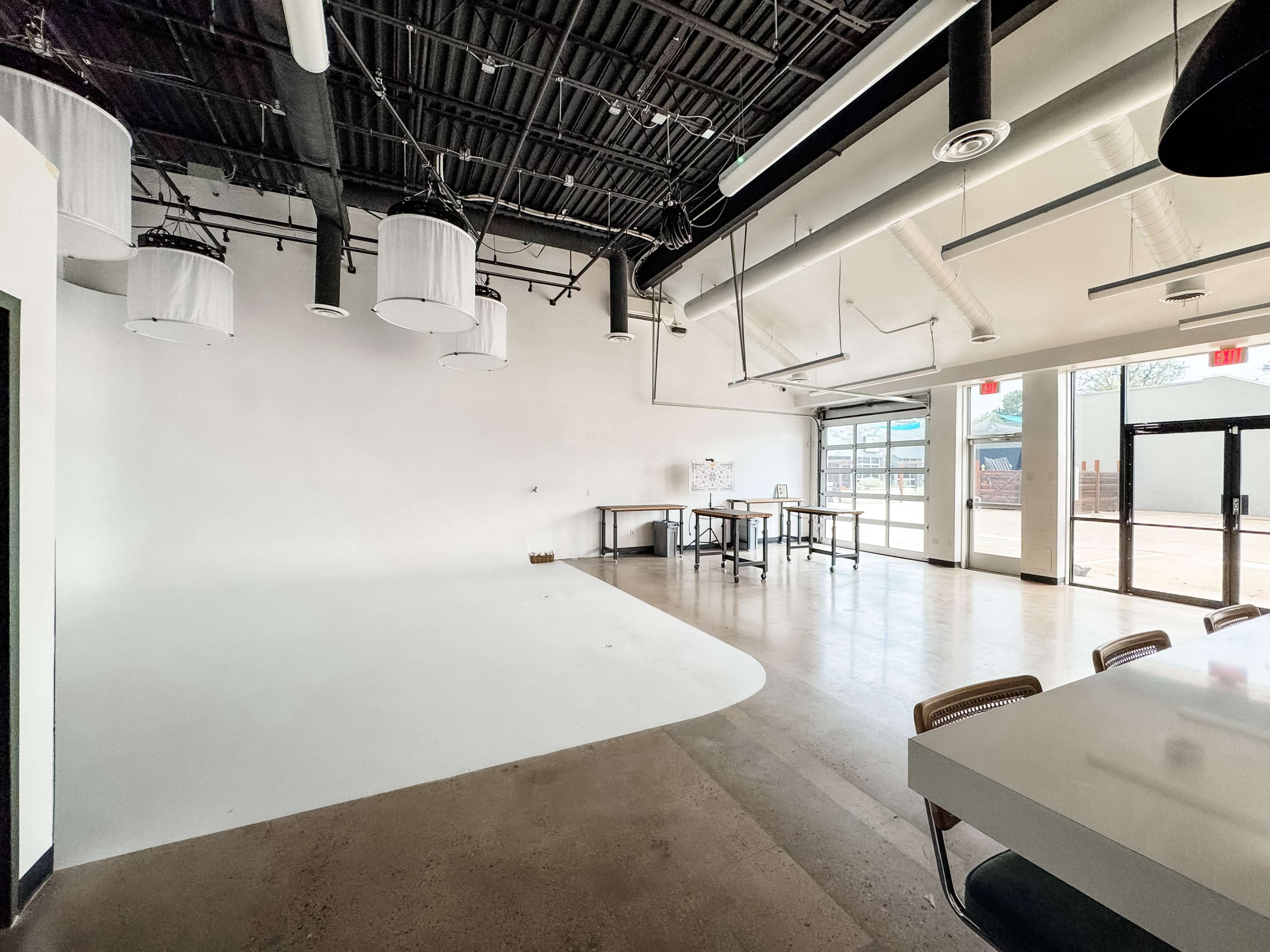The image shows an empty, modern interior space with white walls, high ceilings, and large windows allowing natural light to enter.