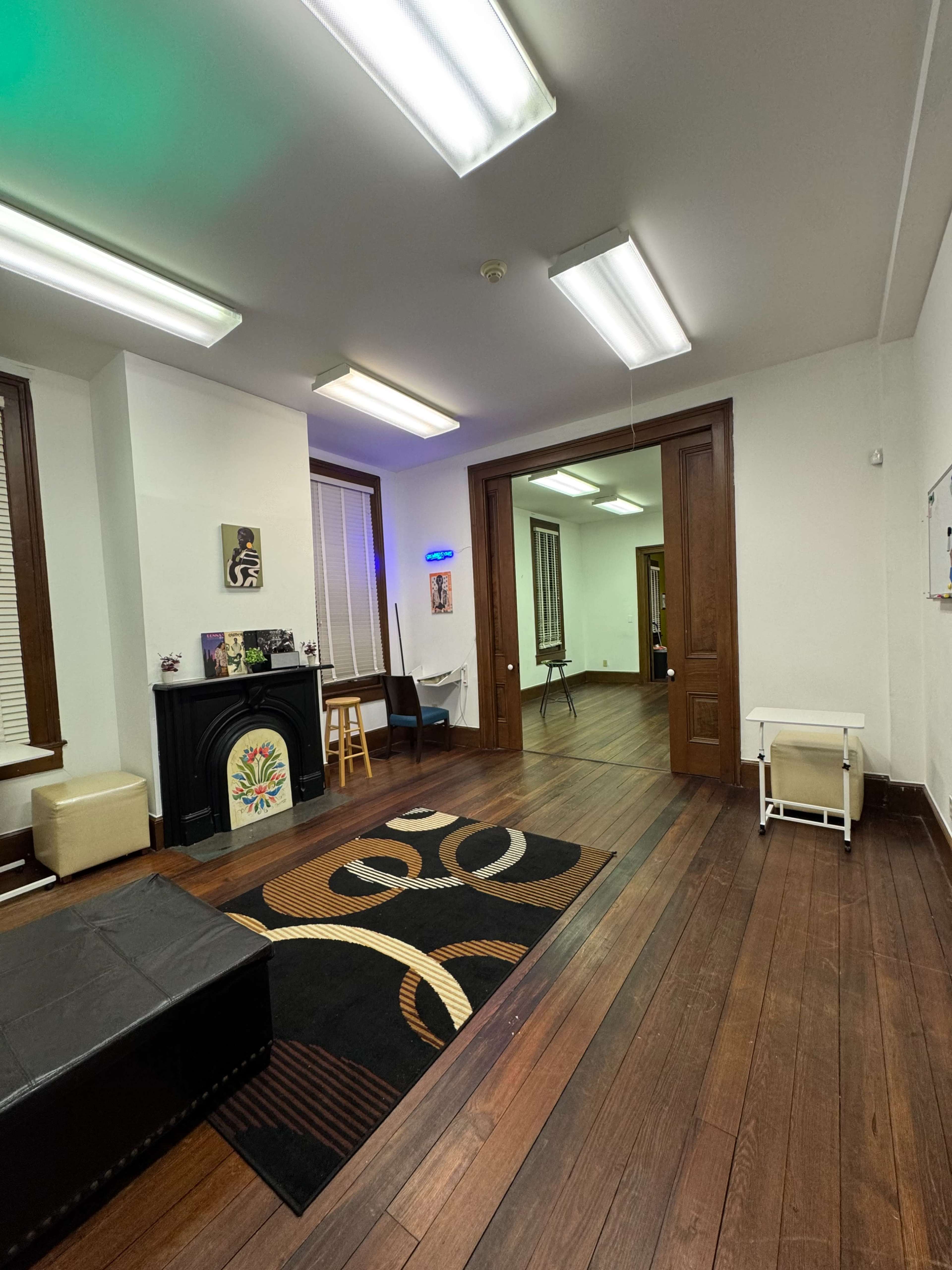The image shows an interior room featuring hardwood floors, a dark rug with a patterned design, a fireplace, and doors leading to another room.