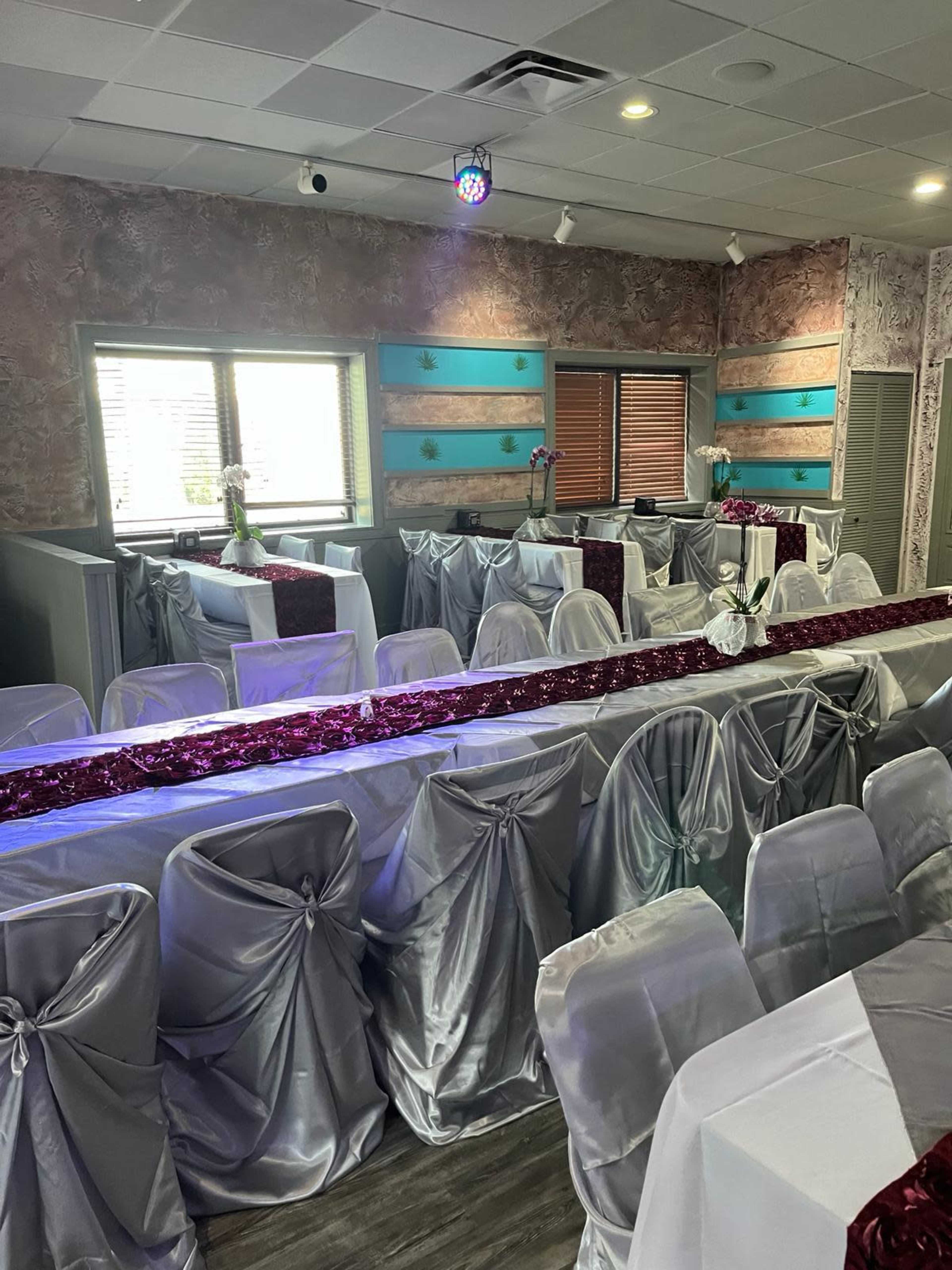 A banquet room is arranged with silver tablecloths and a decorative red runner, featuring tables set for an event under a disco ball.