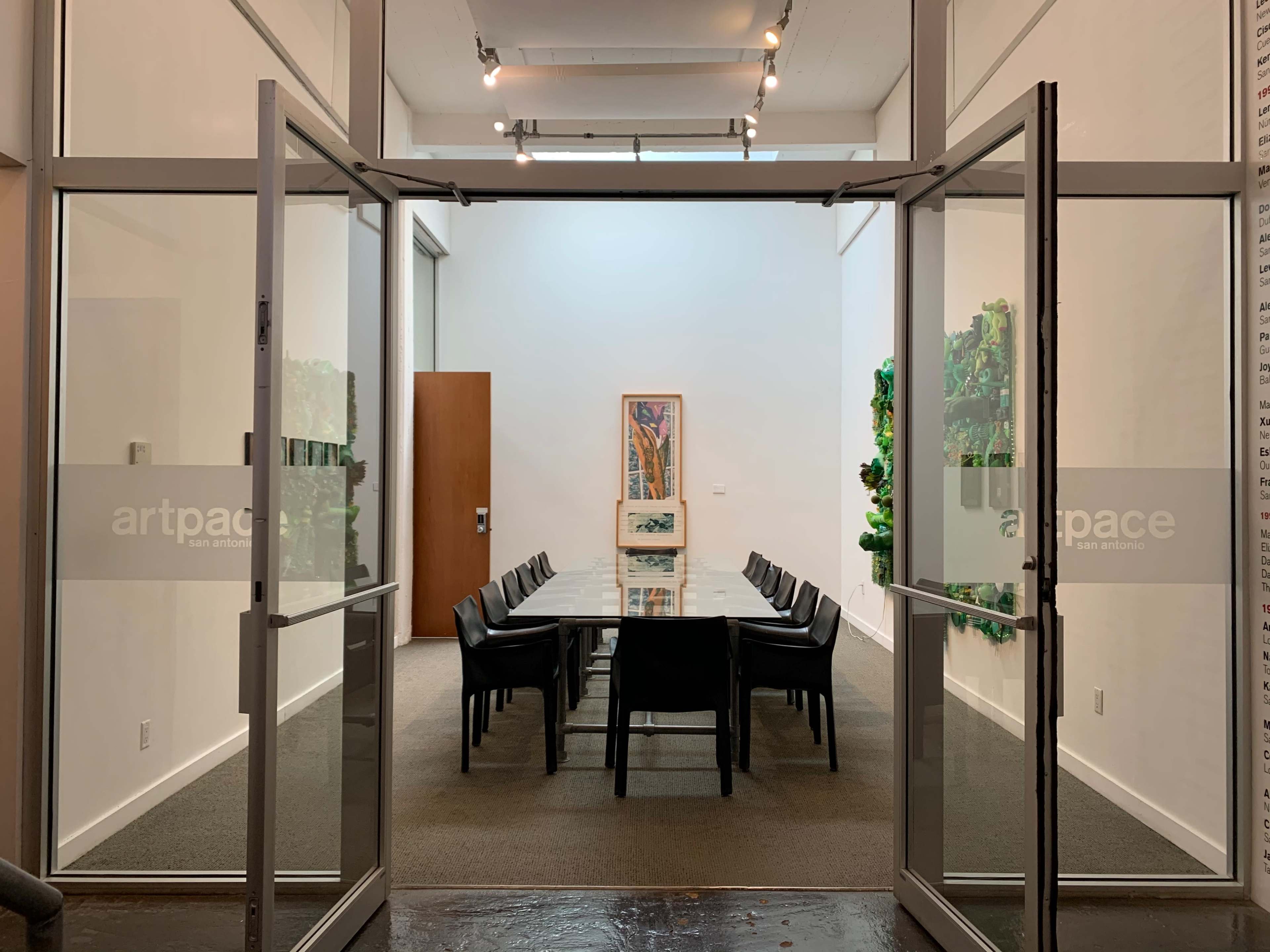The image shows a modern conference room with a glass table and black chairs, visible through open sliding doors.