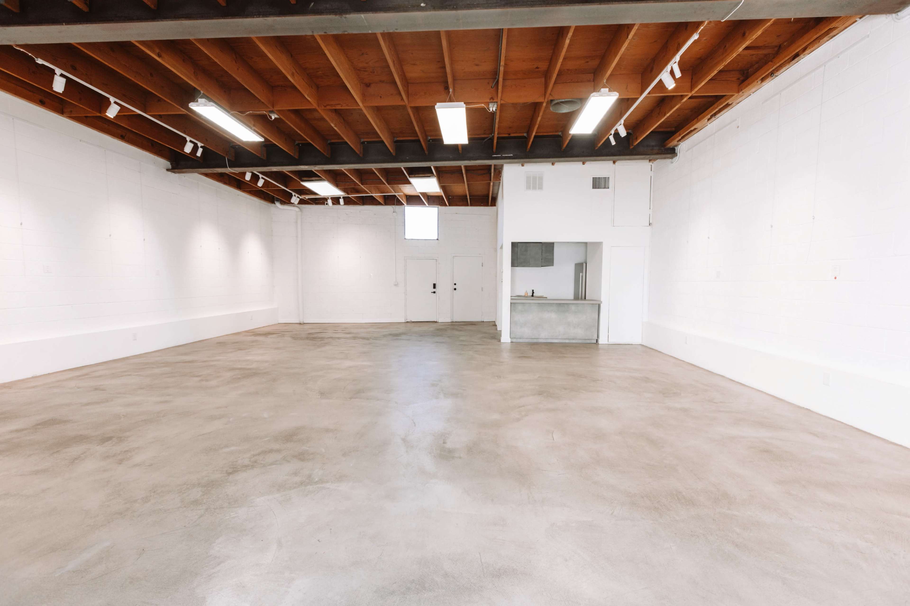 The image shows an empty industrial-style room with polished concrete floors and exposed wooden beams overhead.