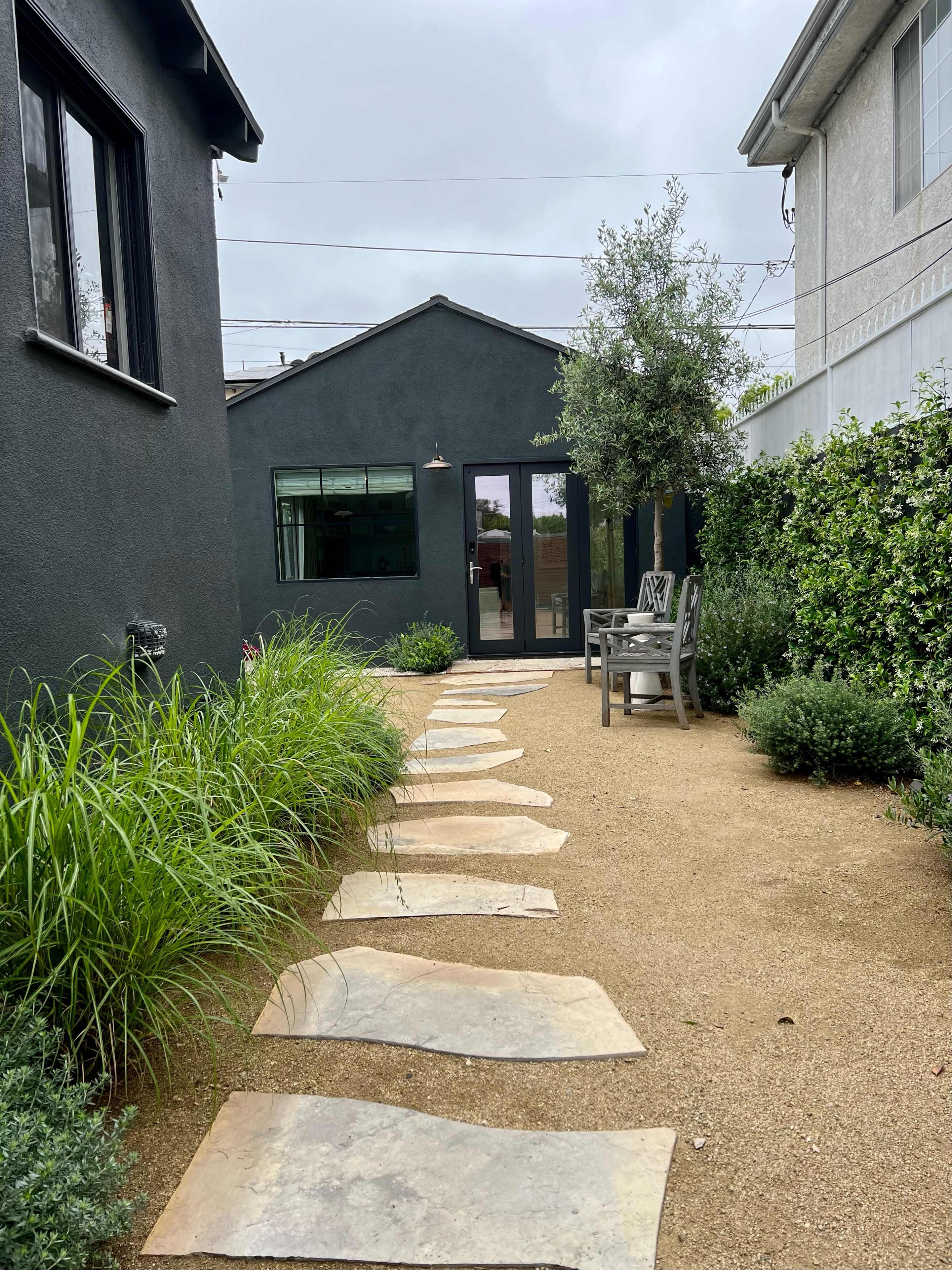 A stone pathway leads through a landscaped garden to a glass-paneled building with a dark exterior.