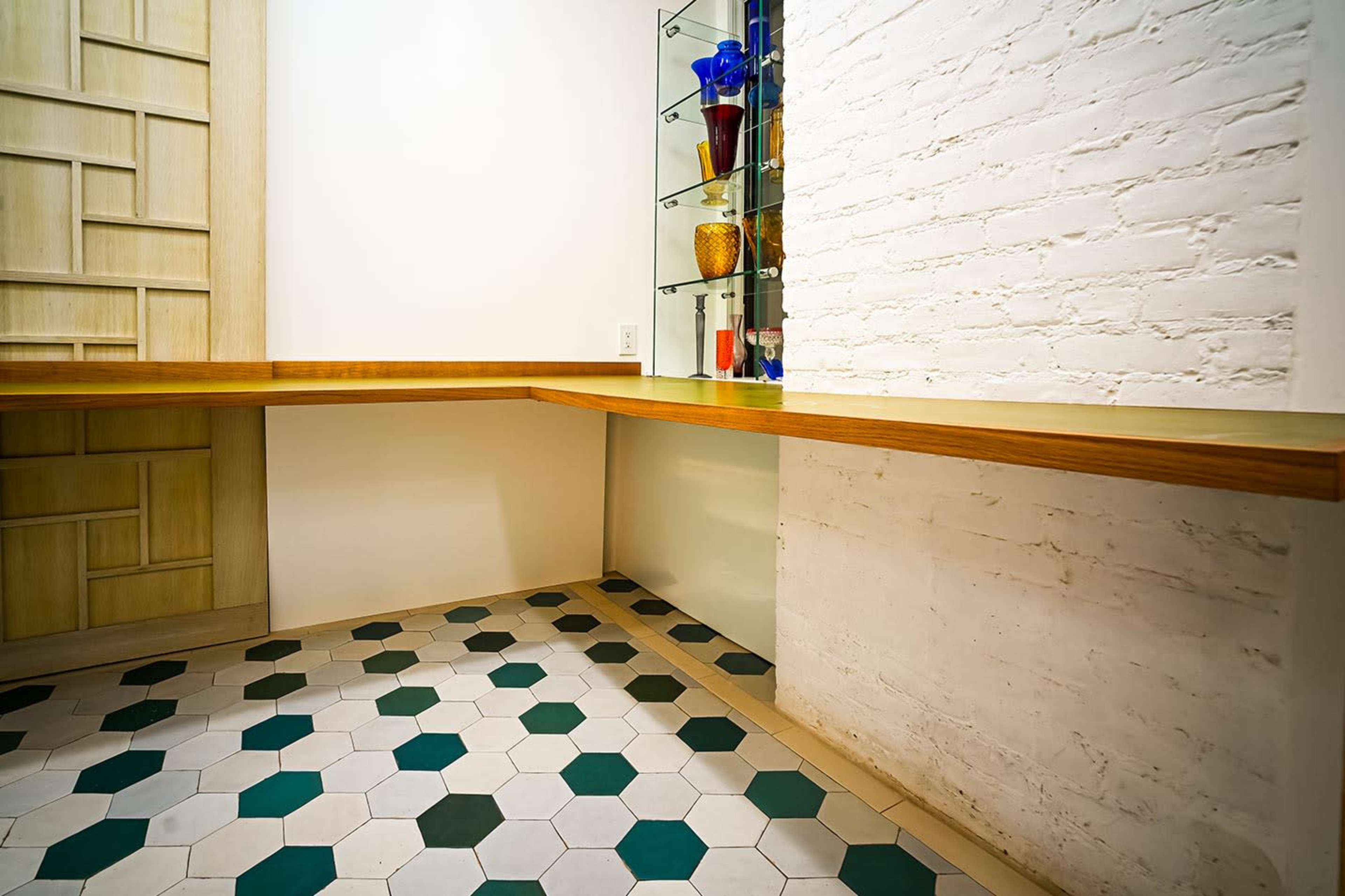 The image shows a corner of a room featuring a wooden countertop and a wall-mounted glass display with colored glass vases.