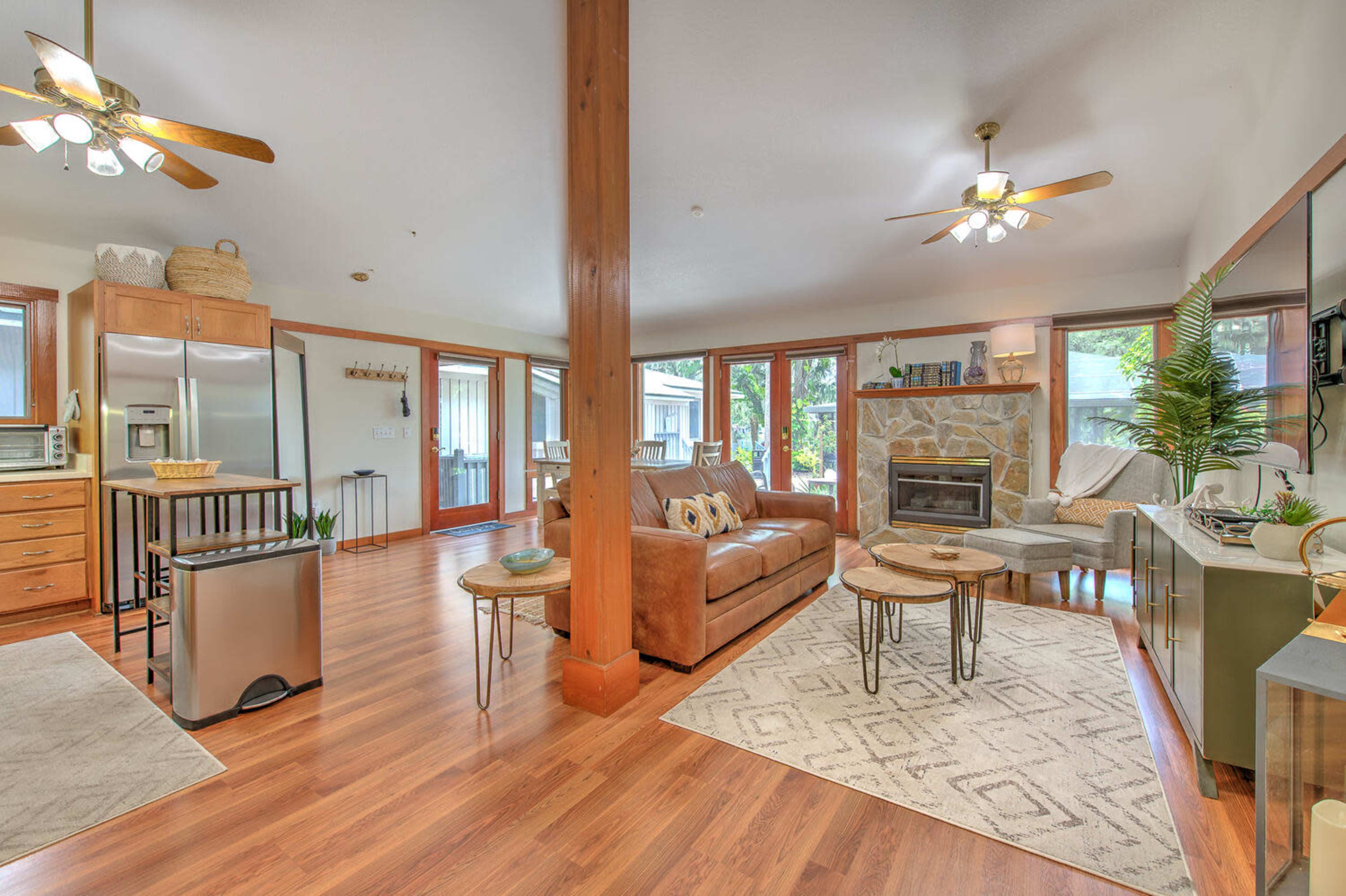 A spacious living room features a comfortable couch, a coffee table set, and a stone fireplace, illuminated by ceiling fans and large windows.