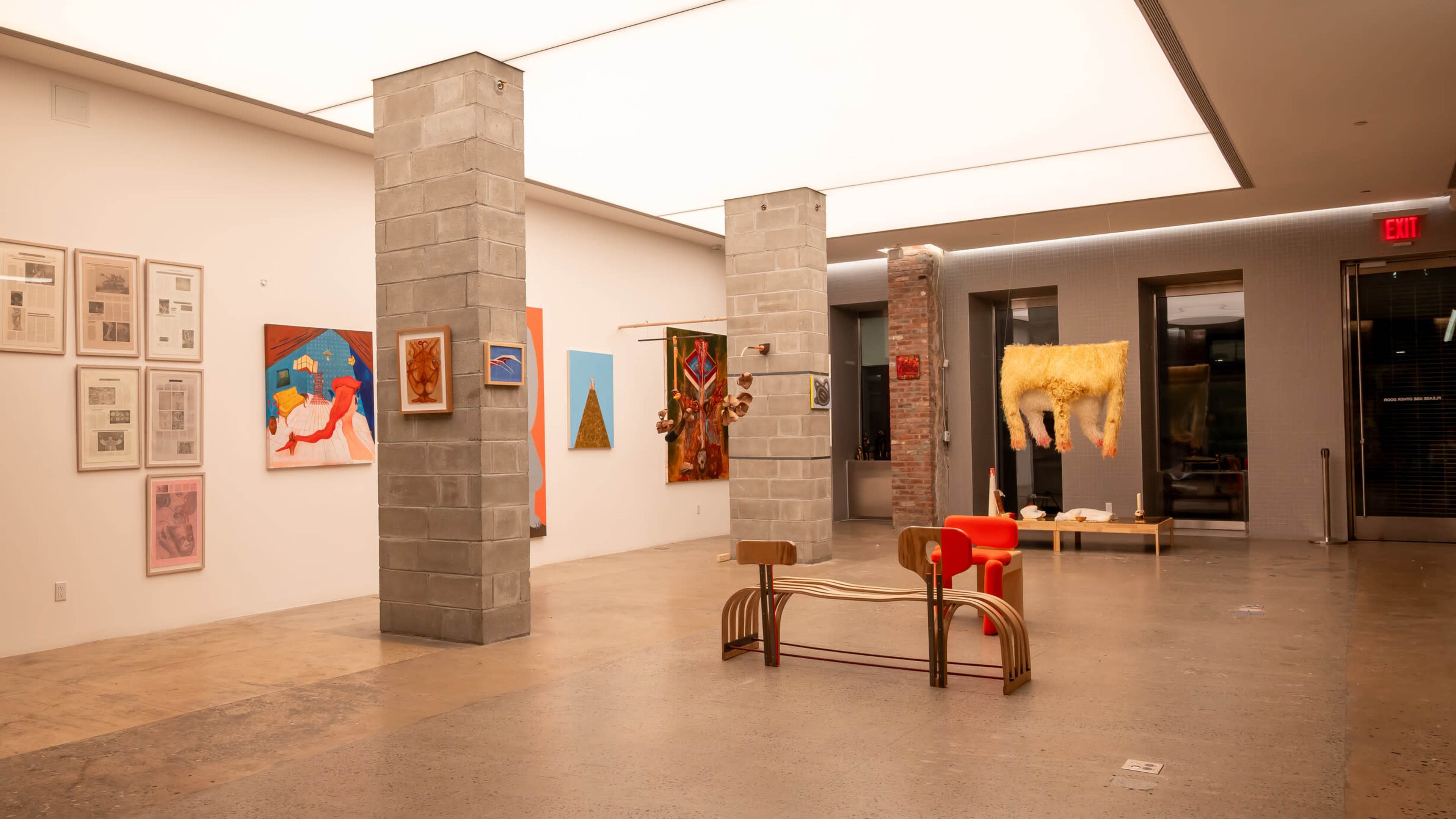 The image shows an art gallery featuring various artworks displayed on the walls, with sculptures and benches in the center of the space.