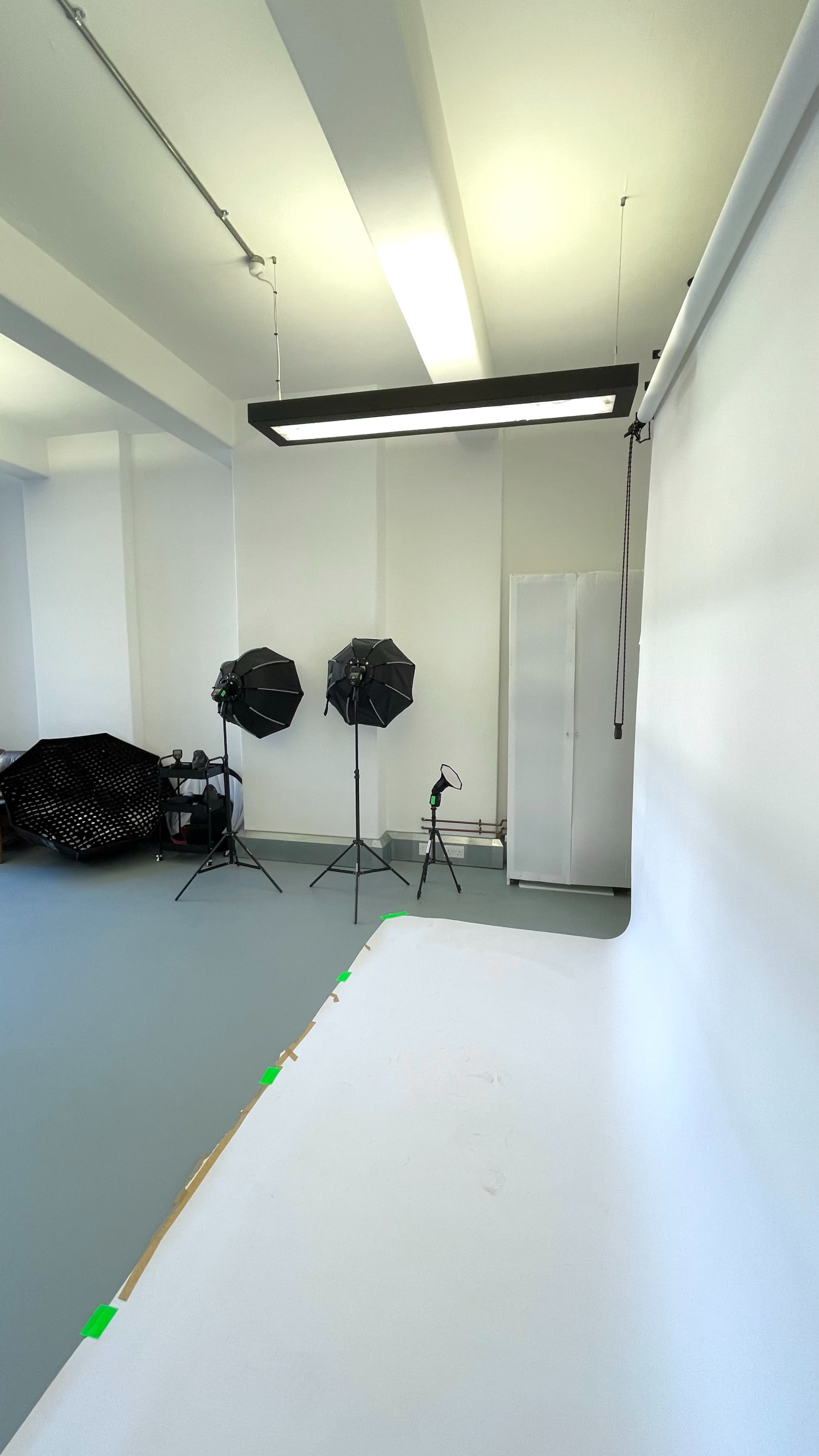 The image shows a spacious photography studio with a white backdrop, two light stands with softboxes, and a metal cabinet in the background.