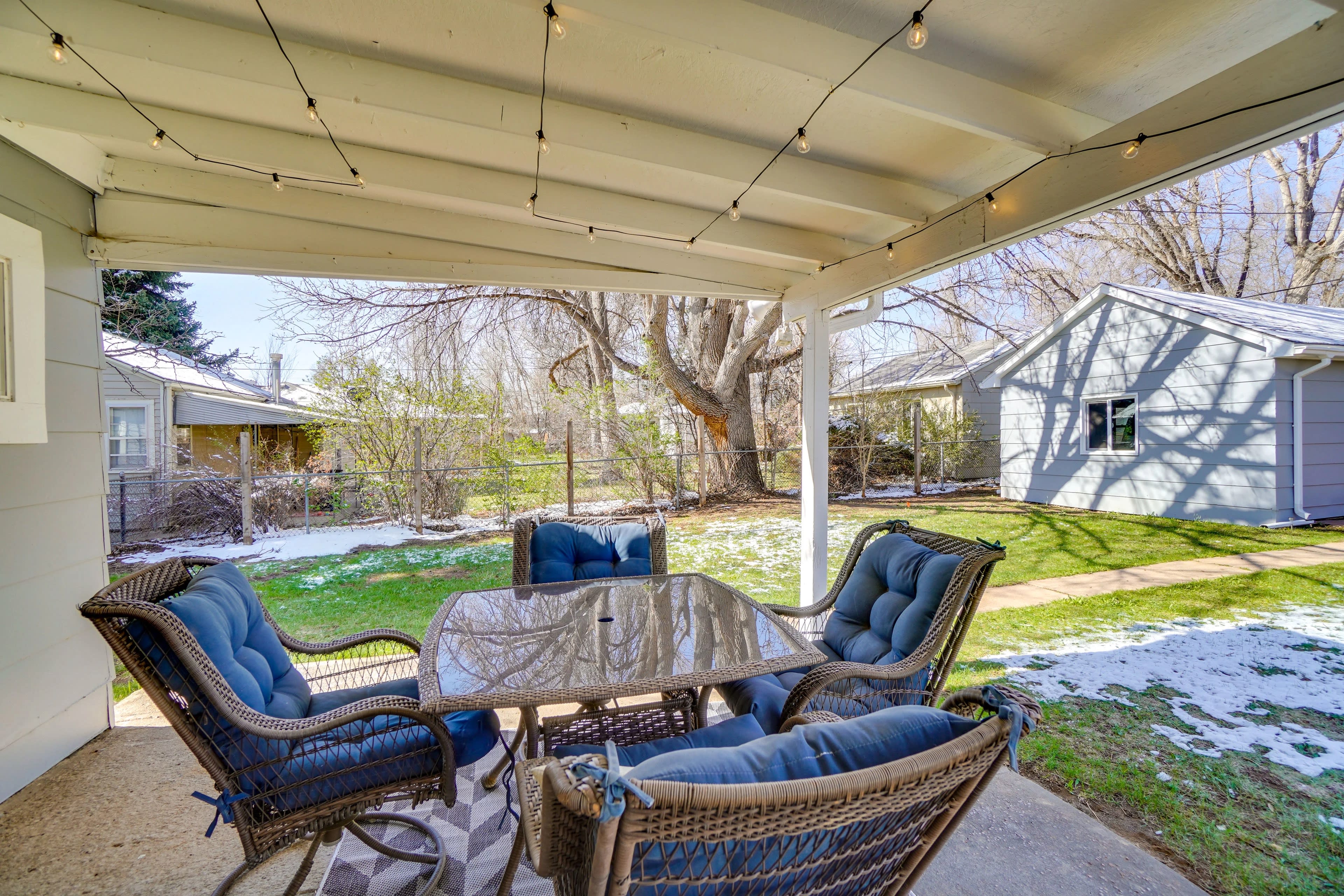 A patio area features a table surrounded by four chairs, with a view of a snowy yard and nearby houses.