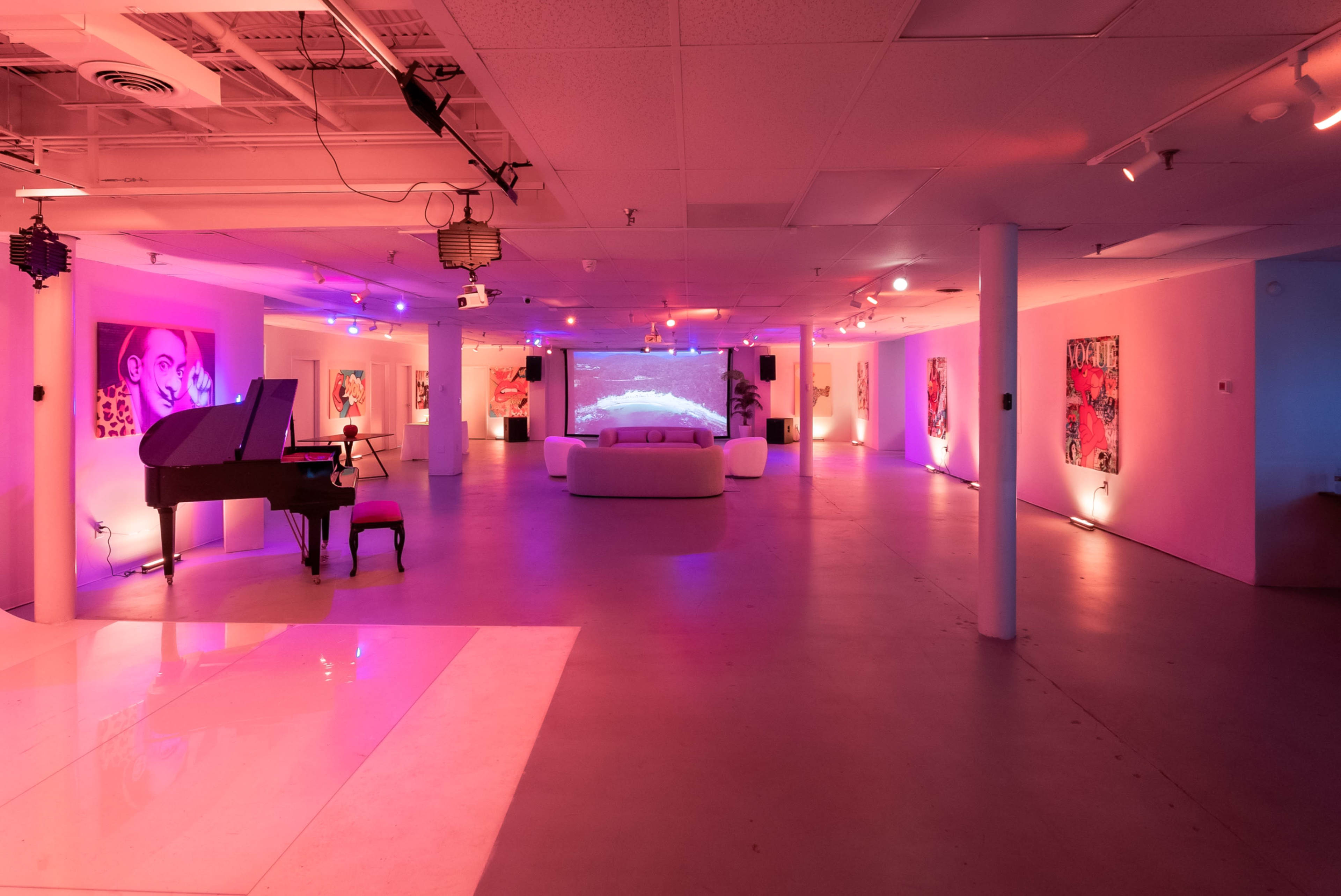 A spacious art gallery features a grand piano, a large projection screen, and walls adorned with colorful paintings, all illuminated by ambient pink and purple lighting.