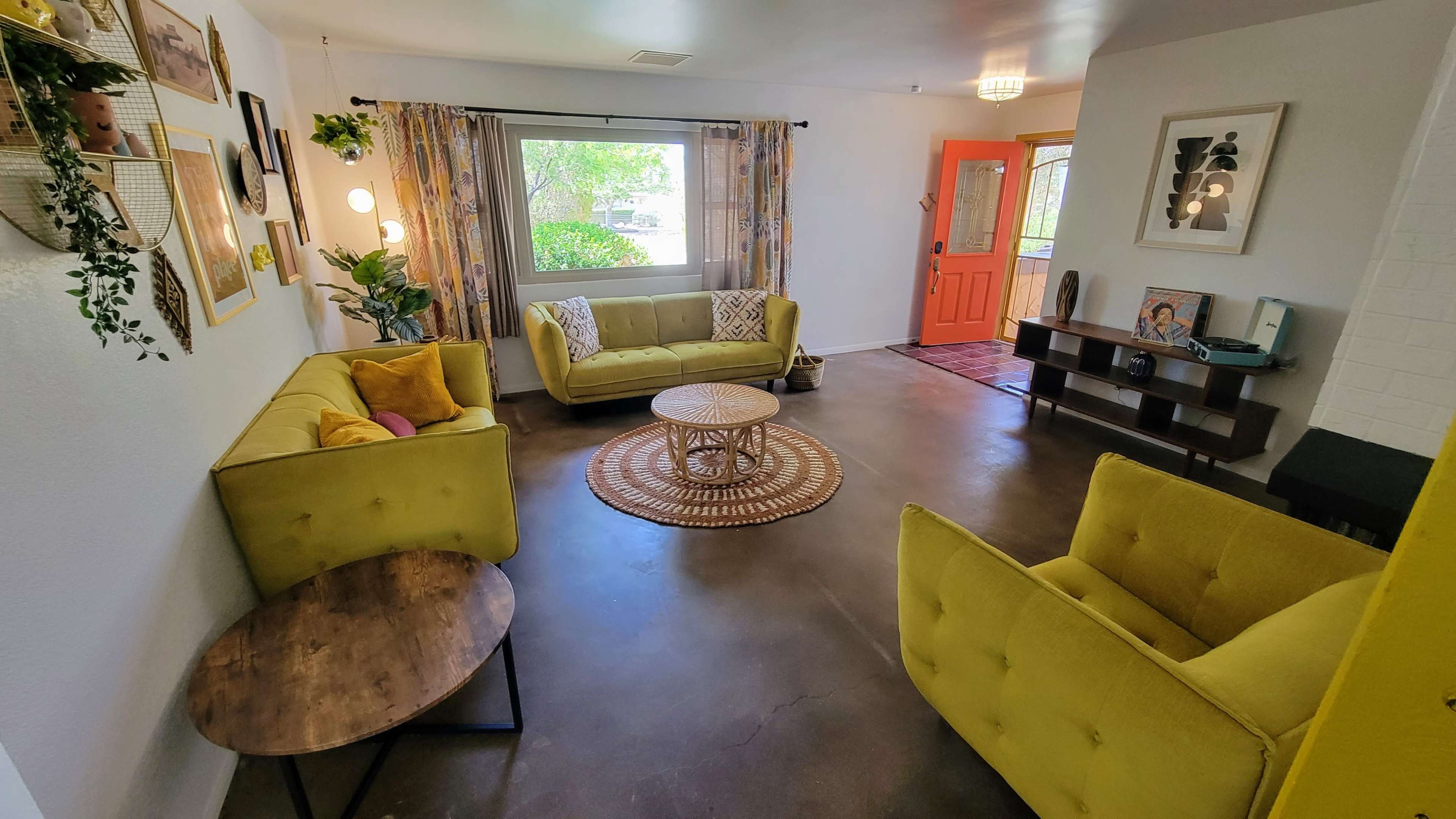 A bright living room features two yellow sofas, a round rug, and a wooden coffee table beside a window with patterned curtains.