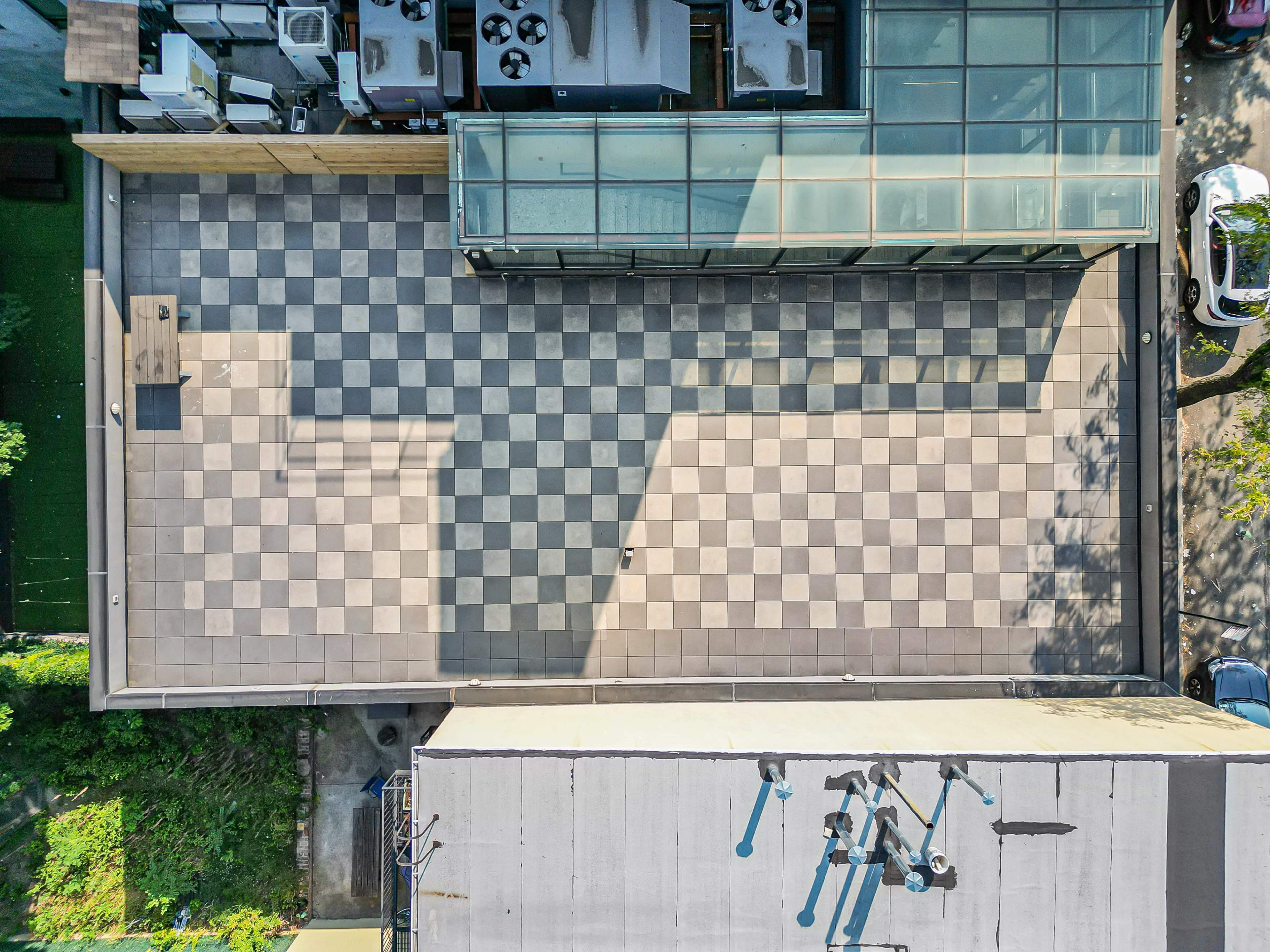 The image shows a rooftop with a checkerboard-patterned floor, surrounded by buildings and greenery.