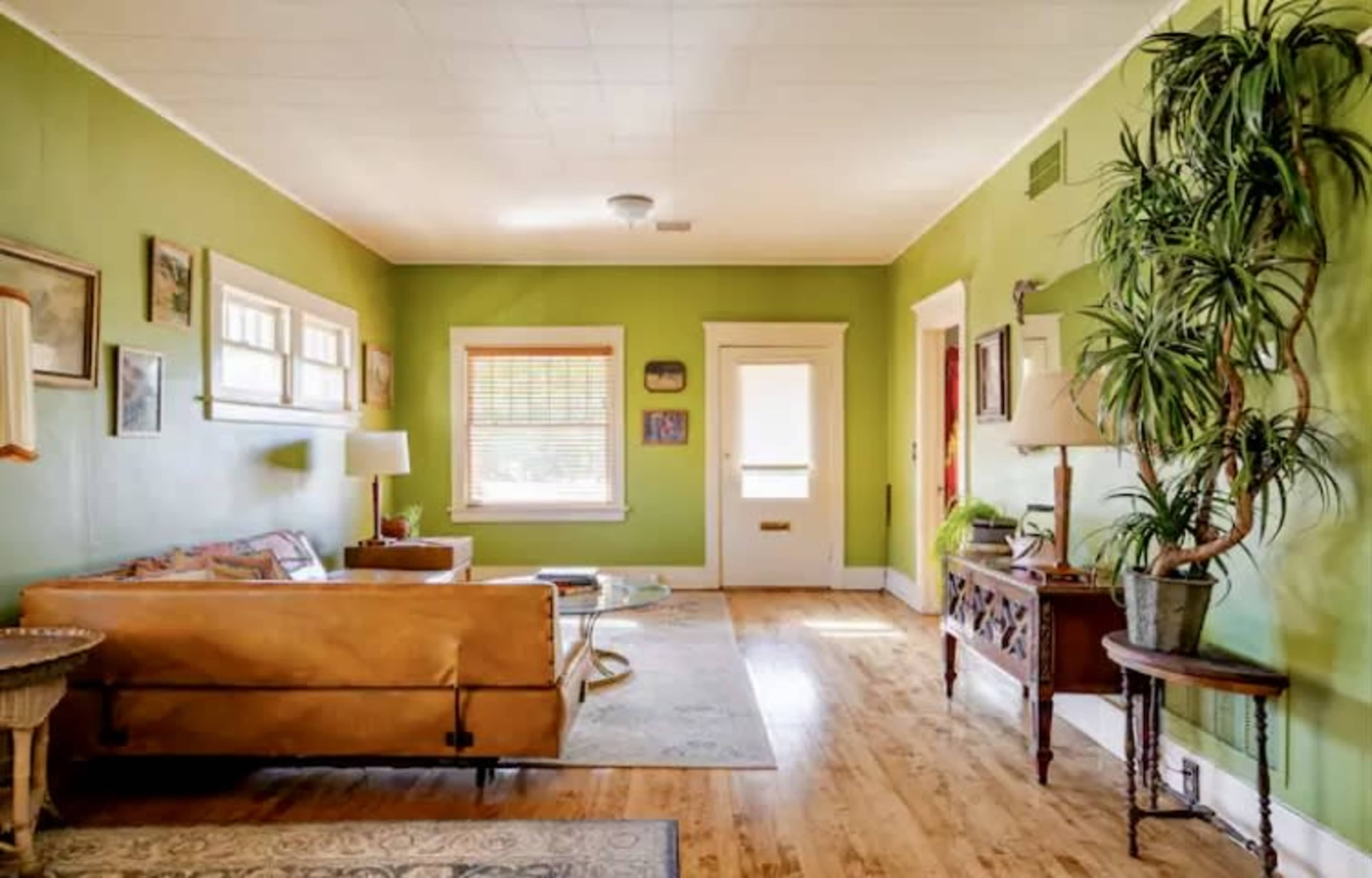 A living room with green walls, a brown couch, a table, a potted plant, and various wall art.