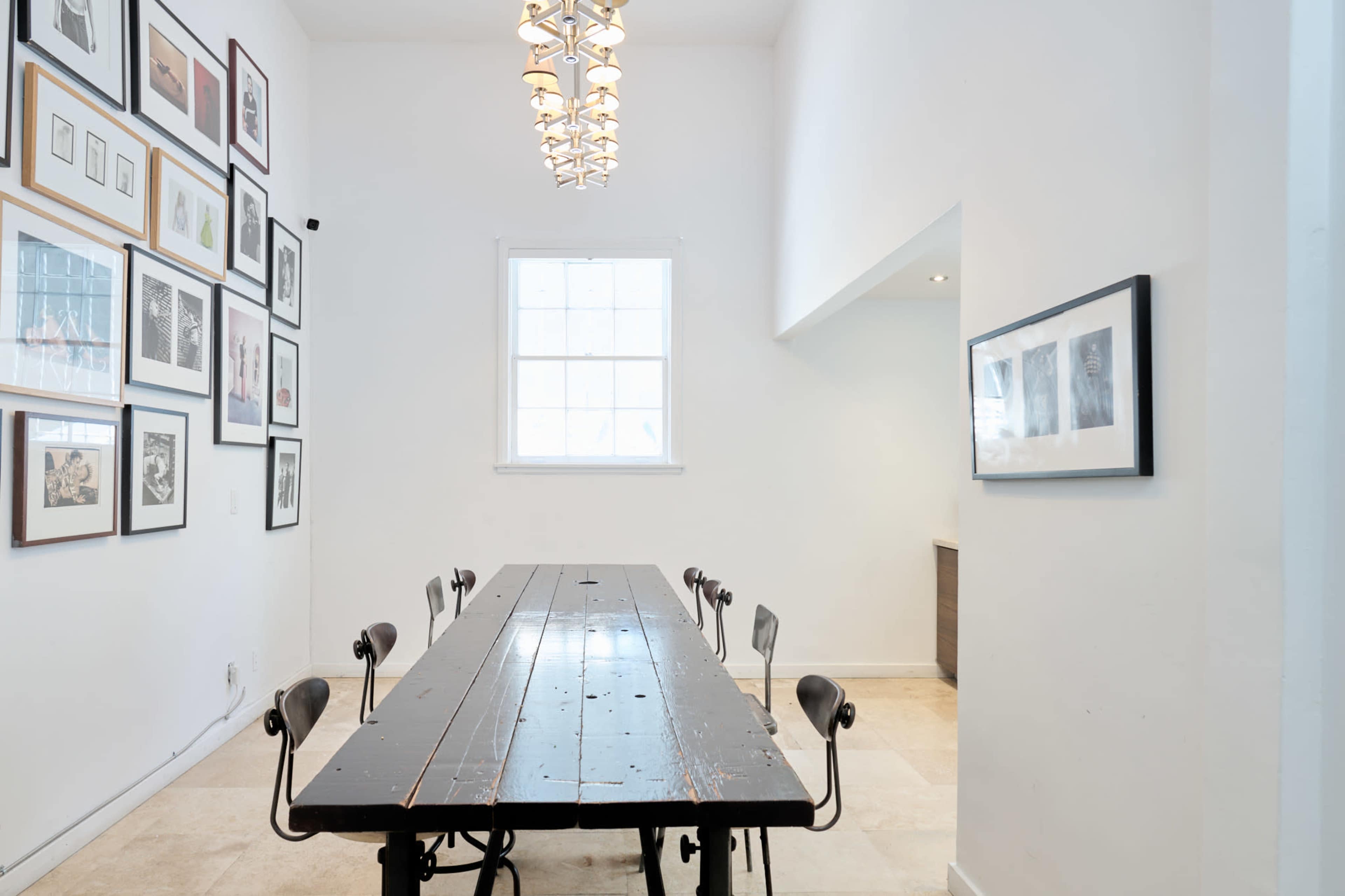 A long, dark wood dining table is positioned in a bright, minimalist room adorned with framed artworks on the walls.