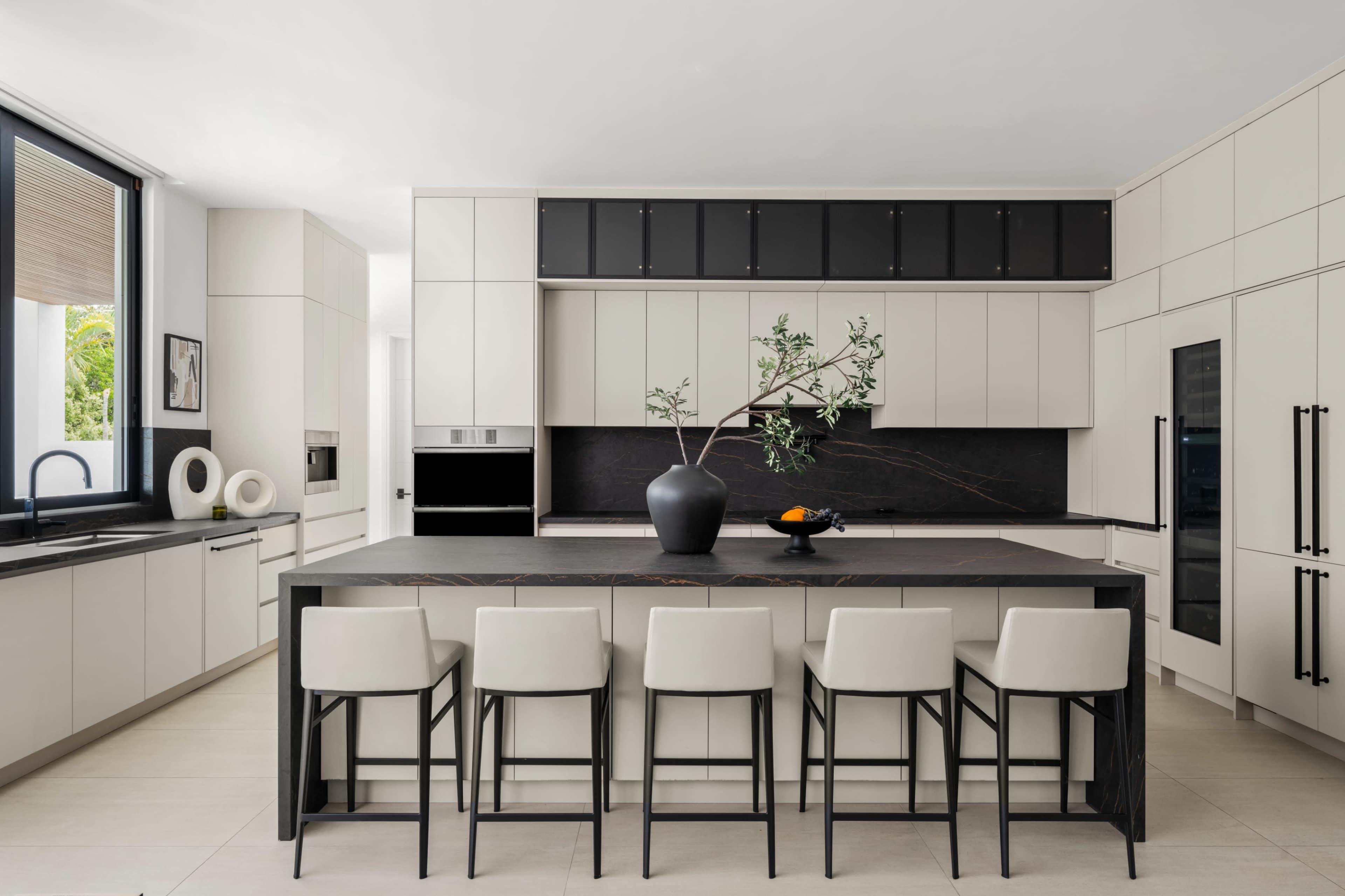 A modern kitchen with a large island, featuring sleek cabinetry in white and black, and a central decorative vase with a branch and fruit.