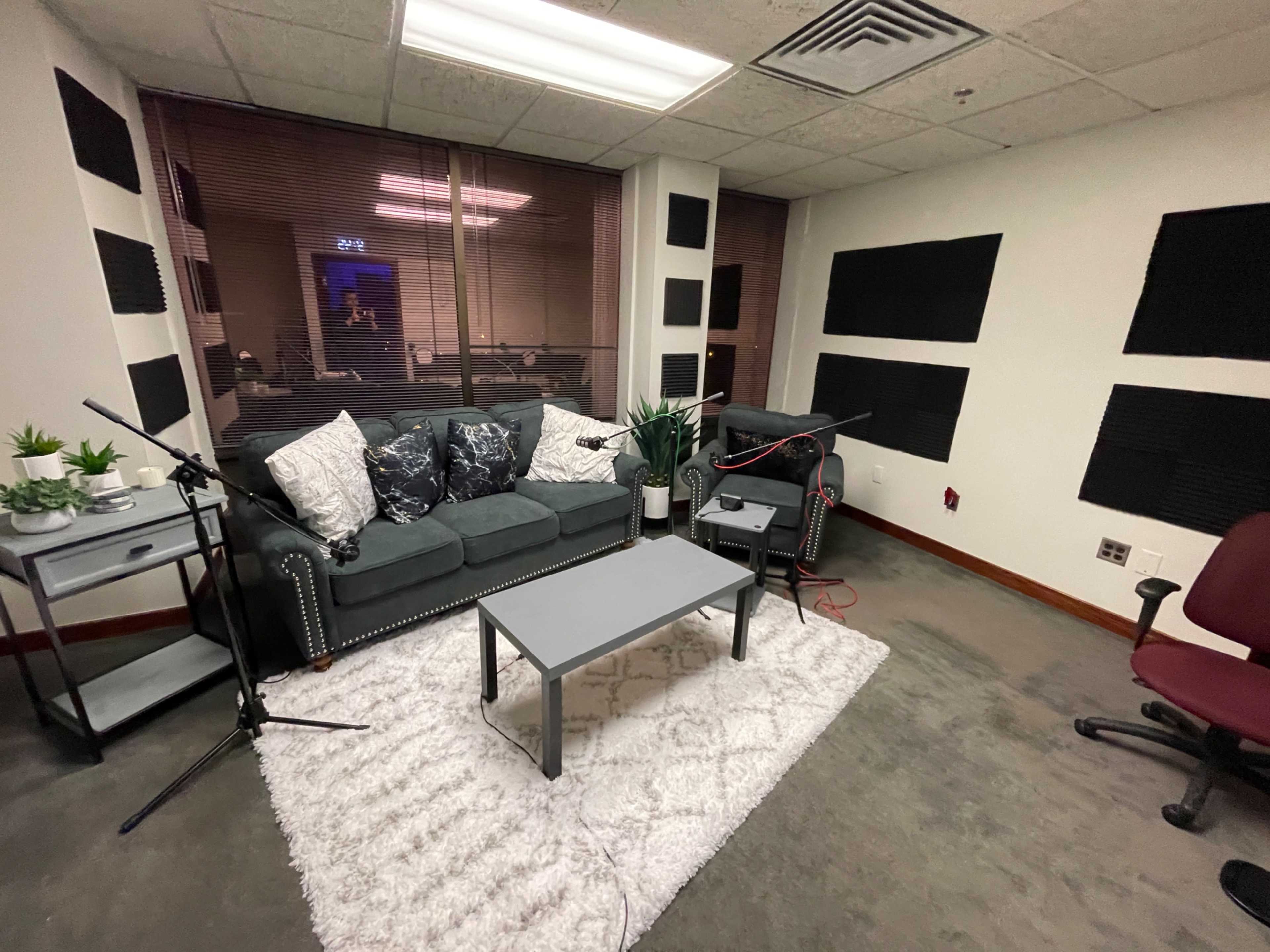 A small recording studio featuring a green couch, a coffee table, and acoustic panels on the walls.