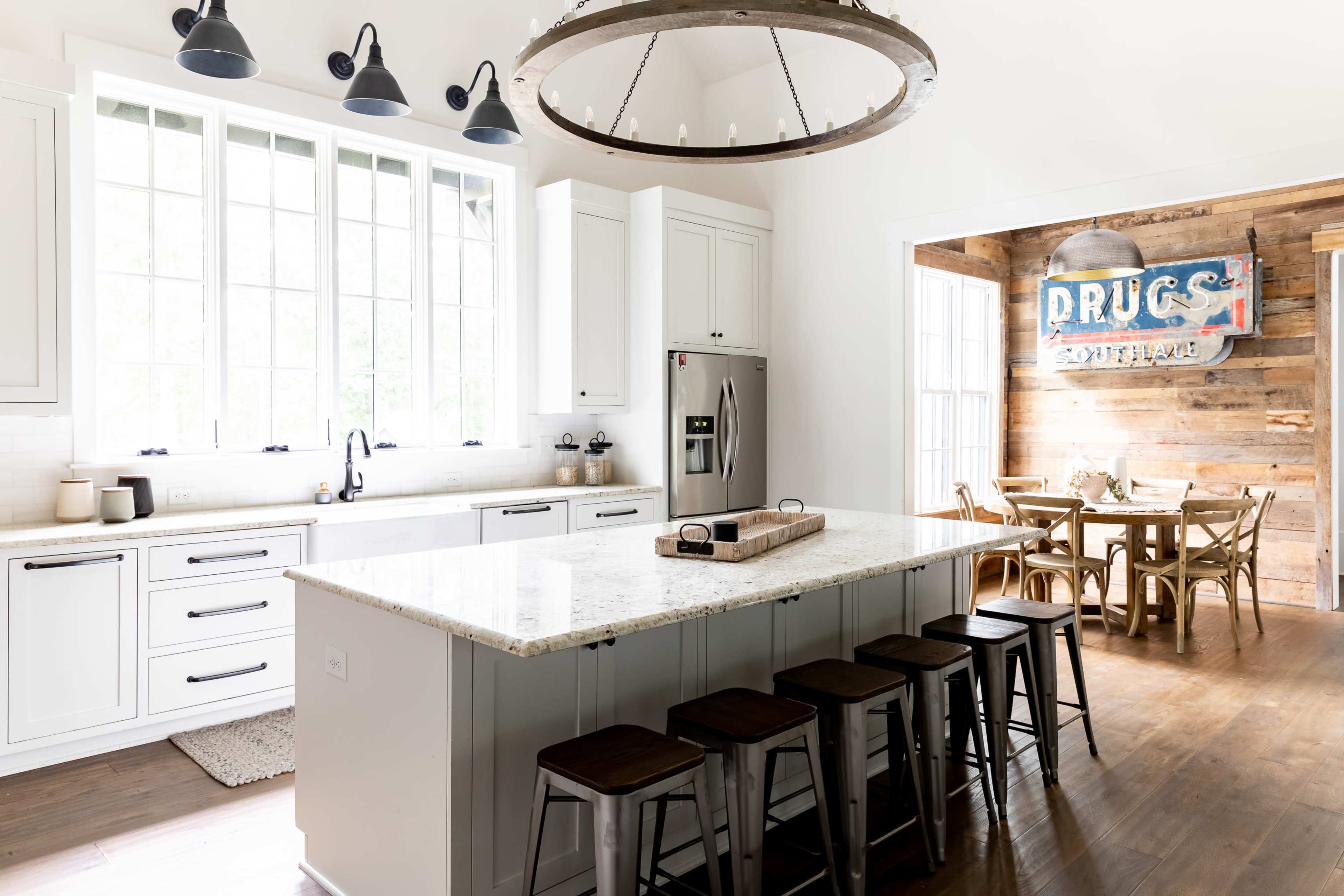 A modern kitchen features a large island with bar stools, stainless steel appliances, and a rustic dining area with a wooden table.