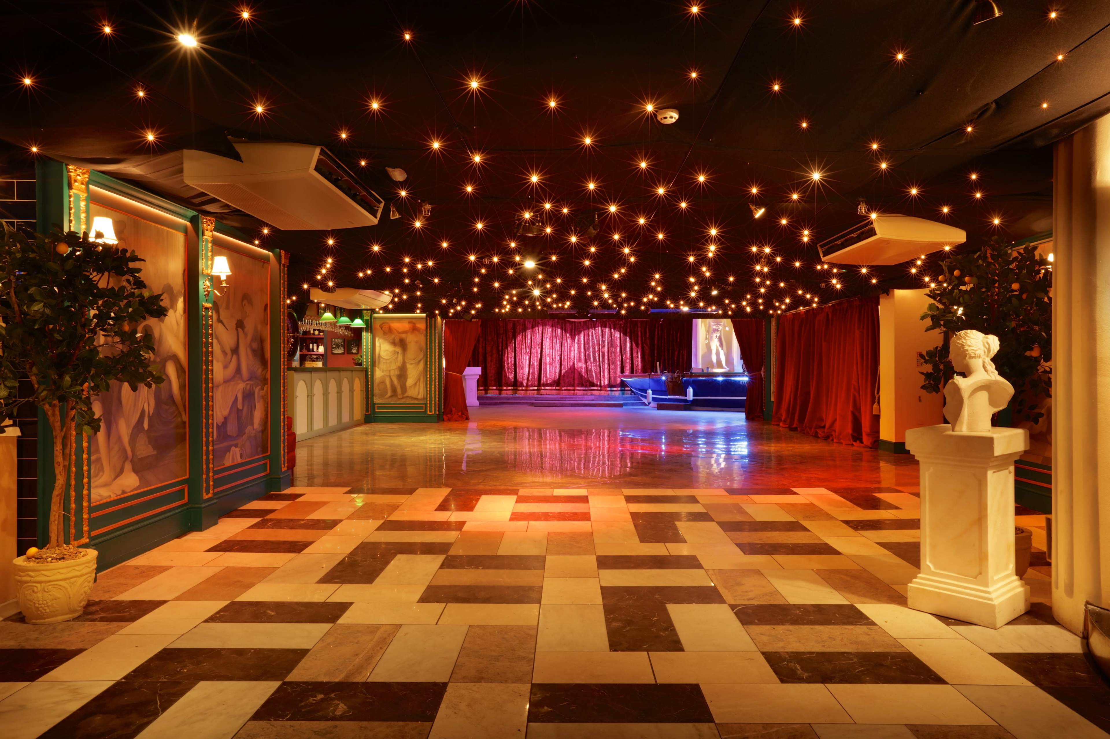 An elegantly designed venue with a checkered floor, decorative walls, and dim lighting featuring a starry ceiling and a stage with red curtains.