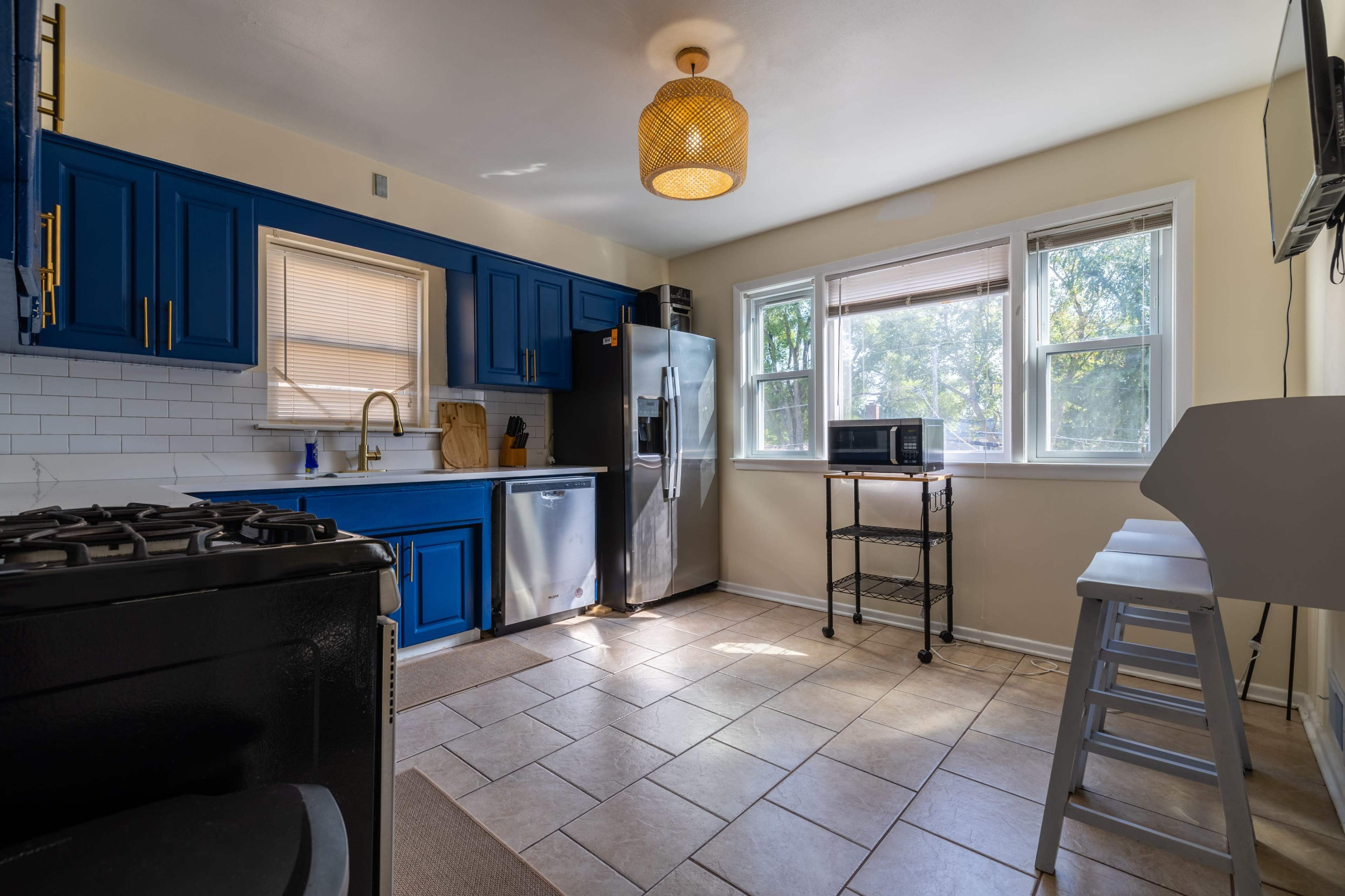 The kitchen features blue cabinets, stainless steel appliances, and a small cart near the window.